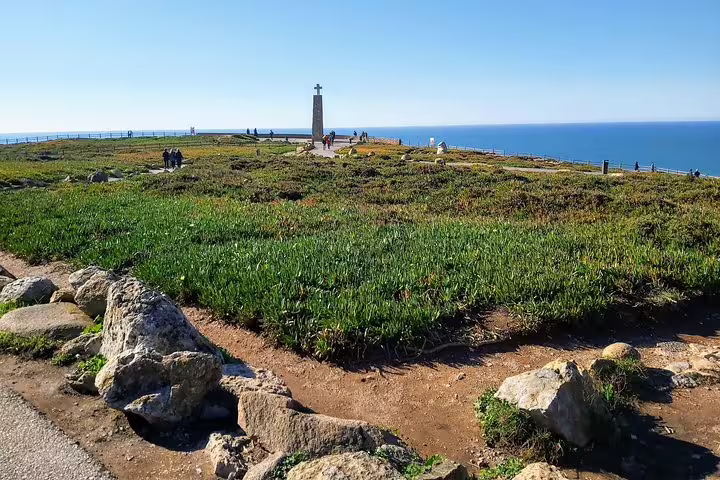 Scenic view of Cabo da Roca's rugged coastline in Sintra, Portugal, showcasing lush greenery and the iconic monument by the sea.