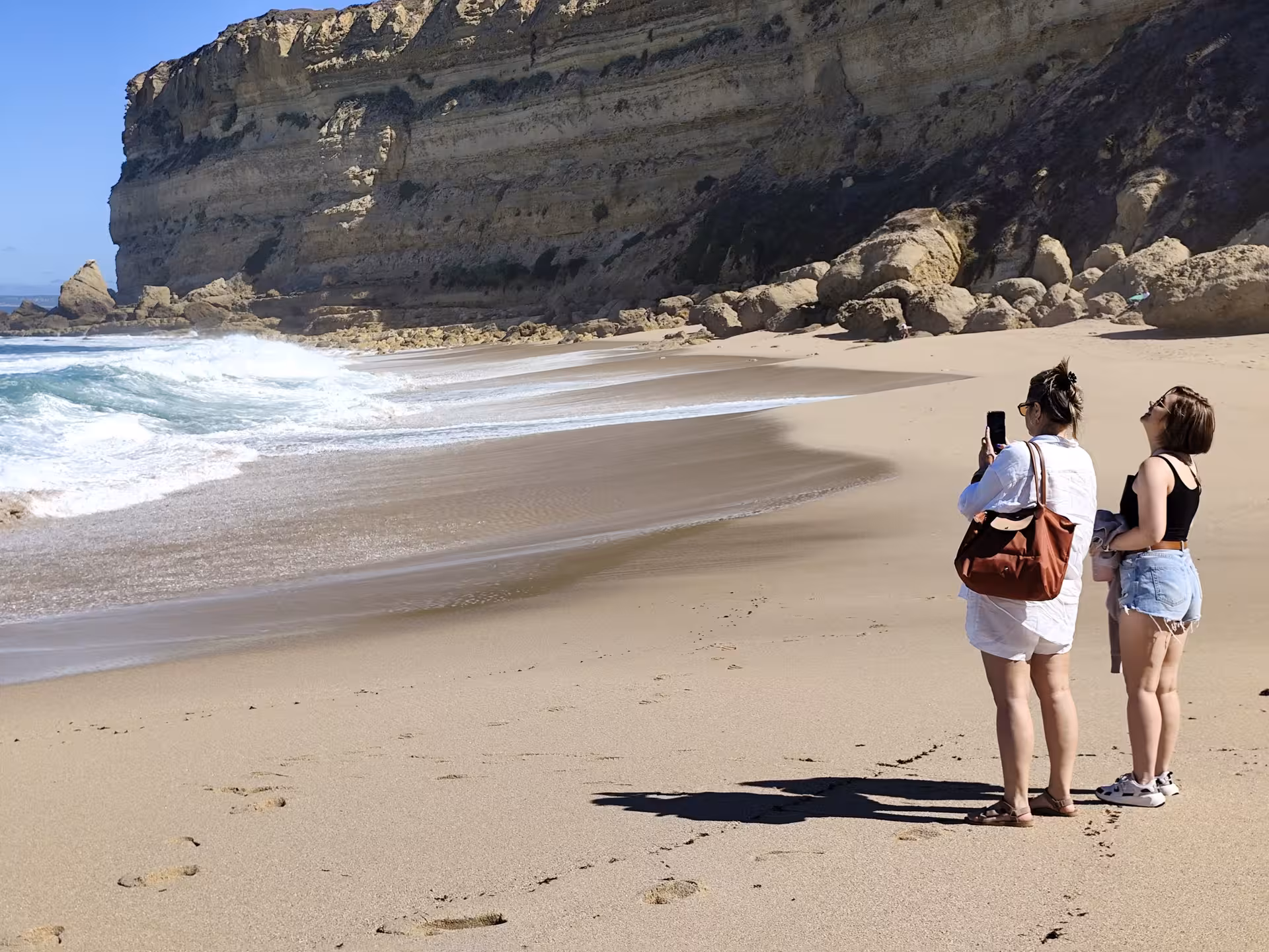 Wild Cabo Espichel tour beach view with Atlantic waves, sandy shore and dramatic limestone cliffs