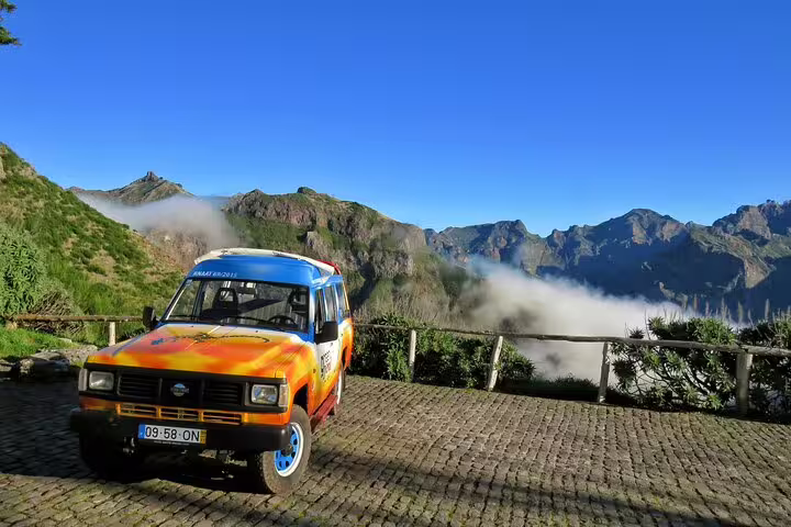 Colorful 4WD vehicle parked on Cabo Girão cliff with stunning mountain and cloud views, ideal for adventure tours in Madeira.