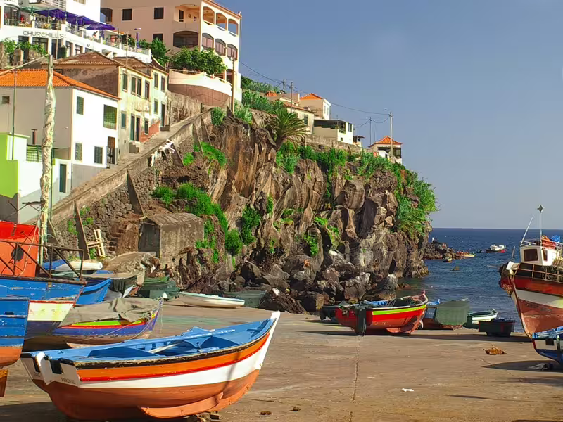 Colorful fishing boats on a scenic coastal dock in Madeira, Portugal, with cliffs and ocean views, perfect for a full-day tour.