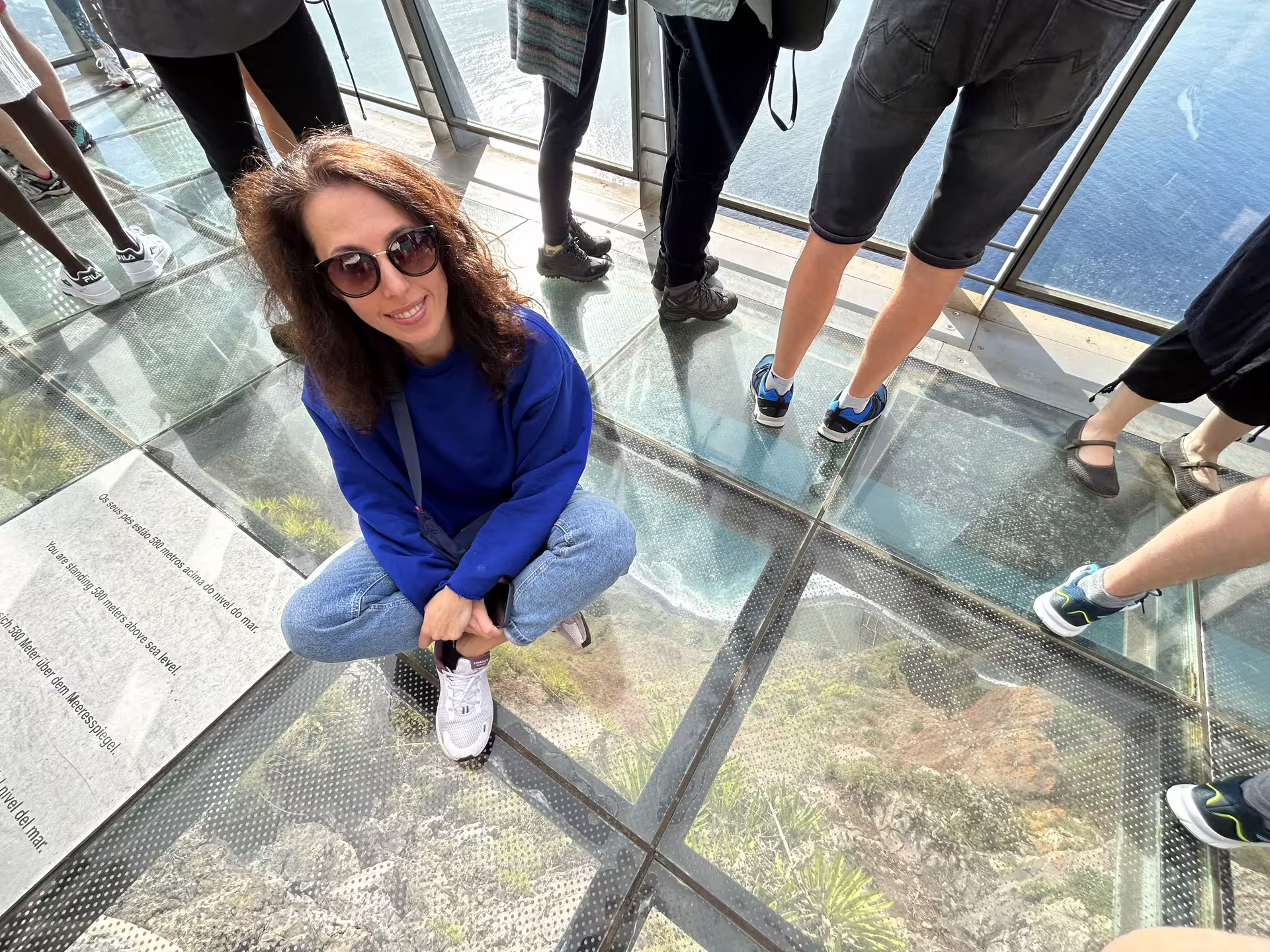 Tourists enjoy the stunning glass-floored skywalk at Cabo Girão, Madeira, offering breathtaking ocean views on a sunny day.