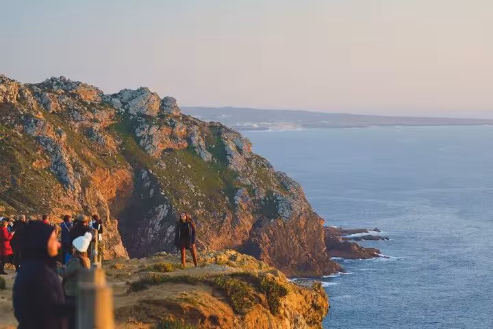 Tourists admire the stunning coastal cliffs at Cabo Roca during a small group tour to Sintra, Pena Palace, and Cascais.