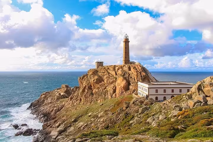 Scenic view of Cabo Vilan lighthouse perched on rocky cliffs overlooking the Atlantic Ocean under a vibrant sky.