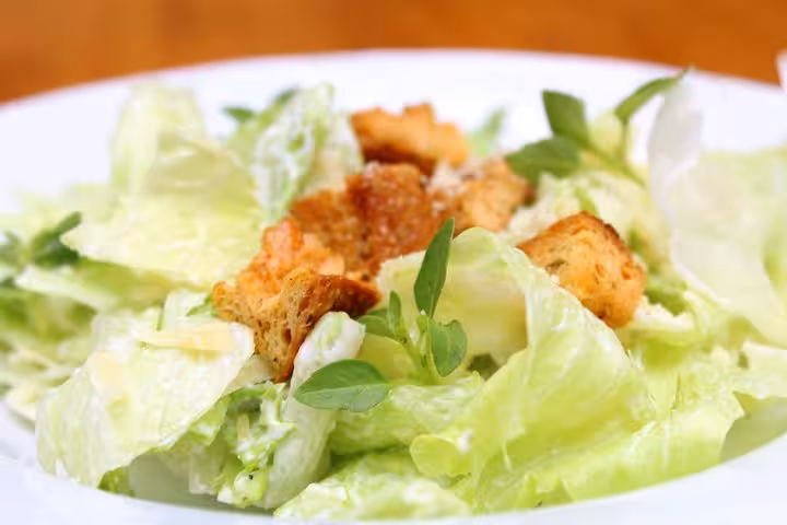 Close-up of a fresh Caesar salad featuring crunchy croutons at a traditional Brazilian diner with live music.