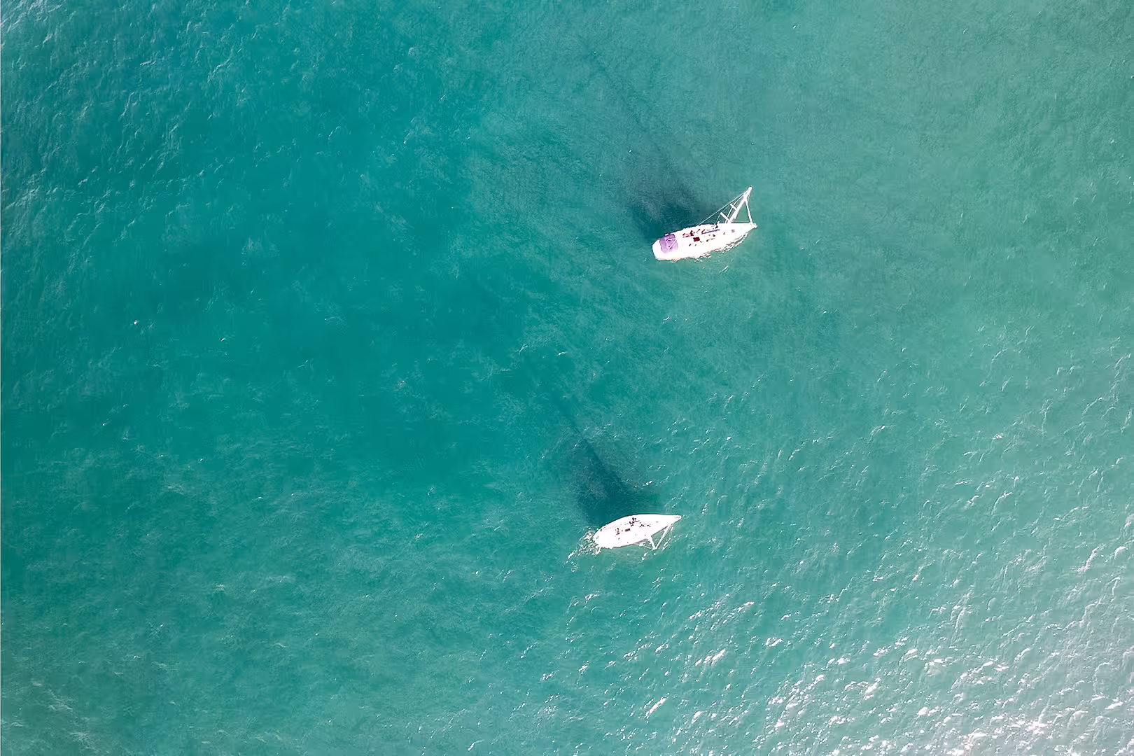 Two sailboats navigating the vibrant turquoise waters of Cagarras Archipelago, viewed from above on a clear day.