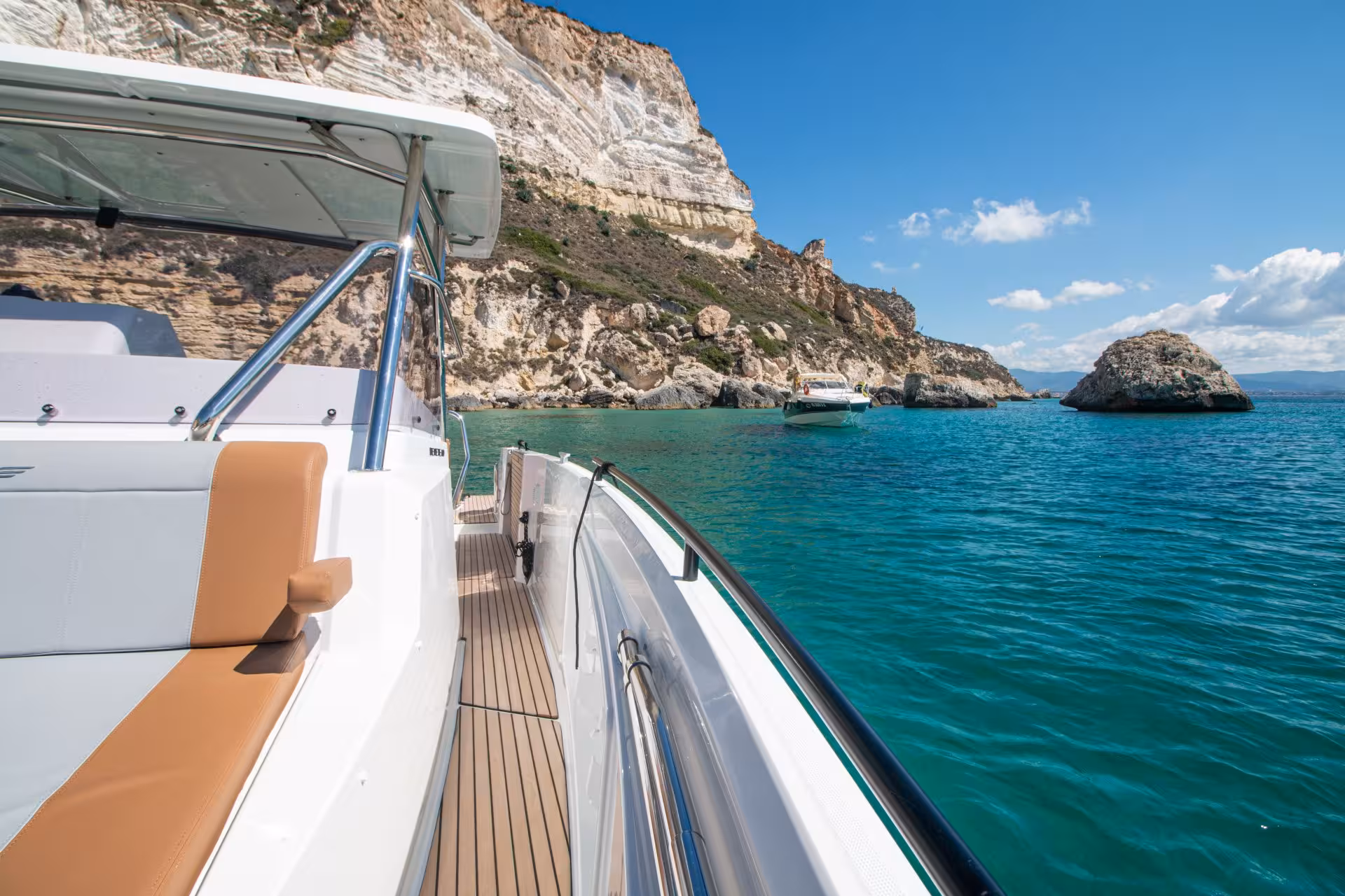 Boat cruising near rocky coastline on Cagliari tour, showcasing stunning cliffs and crystal-clear waters.