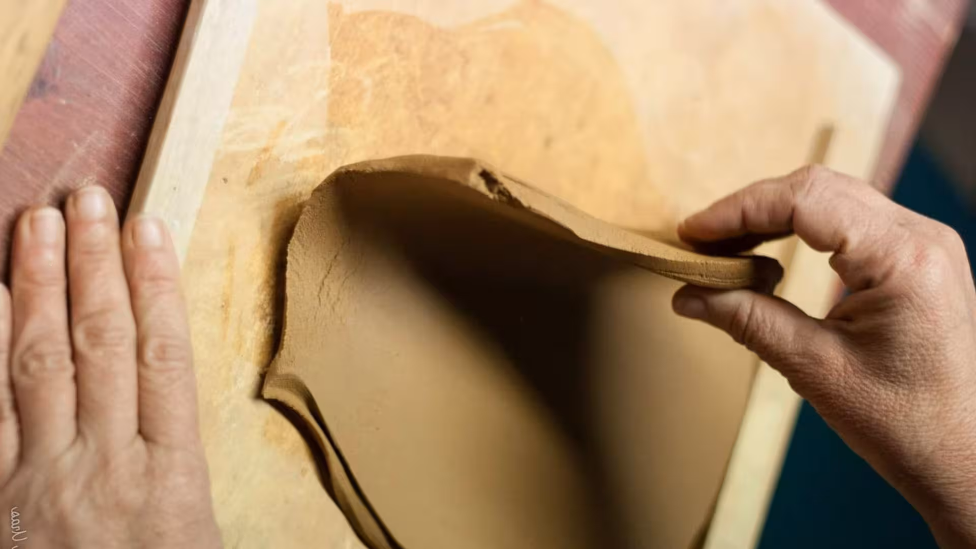 Hands shaping a sheet of clay on a wooden board during a Cagliari ceramics workshop.