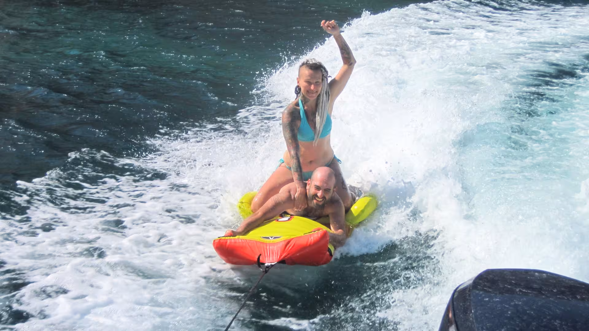 Excited couple having fun on a towable tube ride in Cagliari's Golfo degli Angeli.
