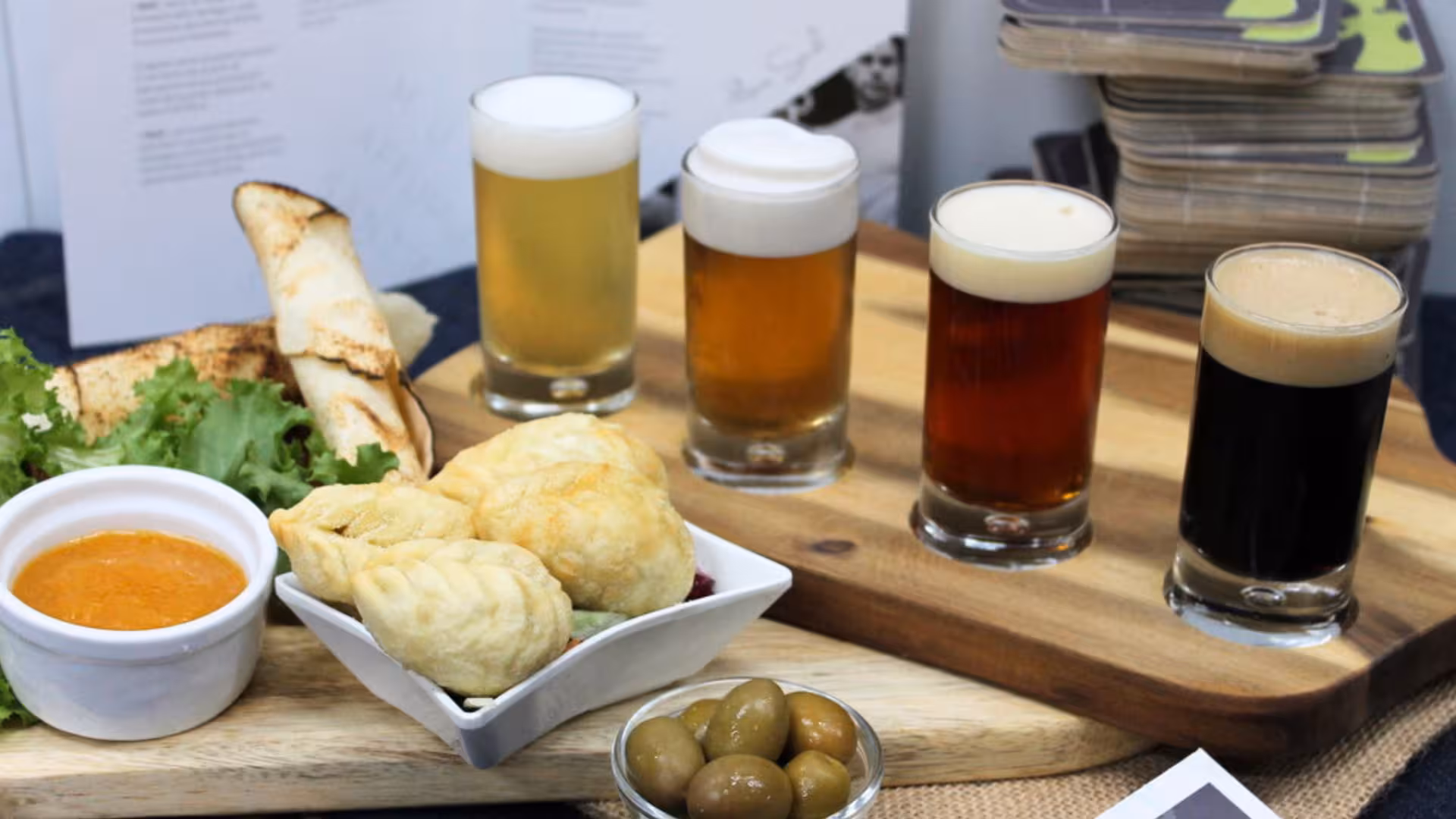 Craft beer tasting in Cagliari featuring five beer samples paired with local snacks and olives on a wooden board.