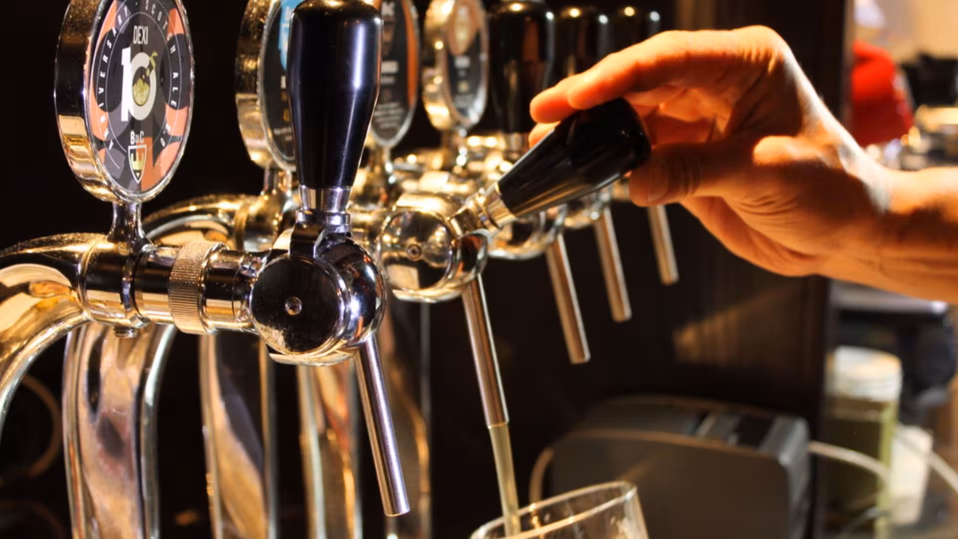 Close-up of a hand pouring beer from a tap at a Cagliari craft brewery, highlighting the artisanal brewing process.
