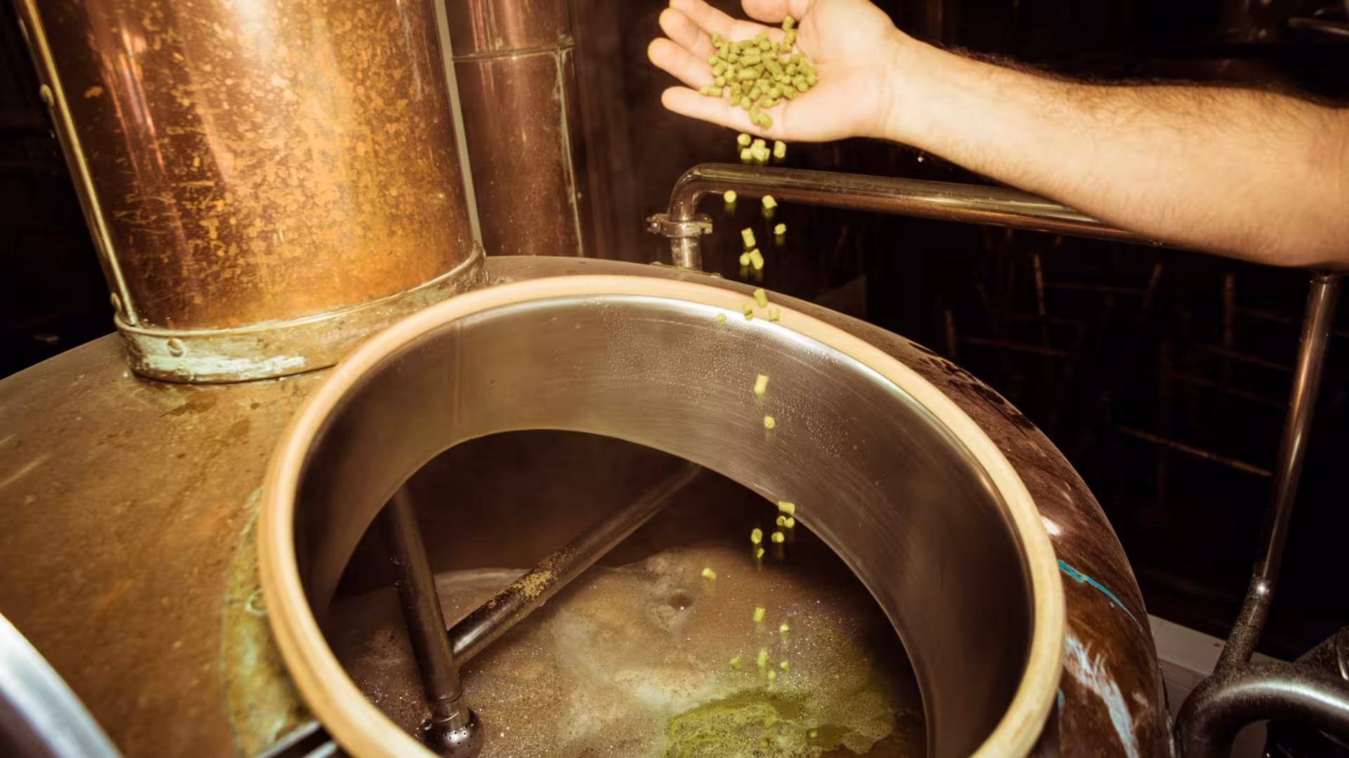 Craft brewer adding hops to a copper kettle in Cagliari's brewery tour, showcasing traditional beer-making process.
