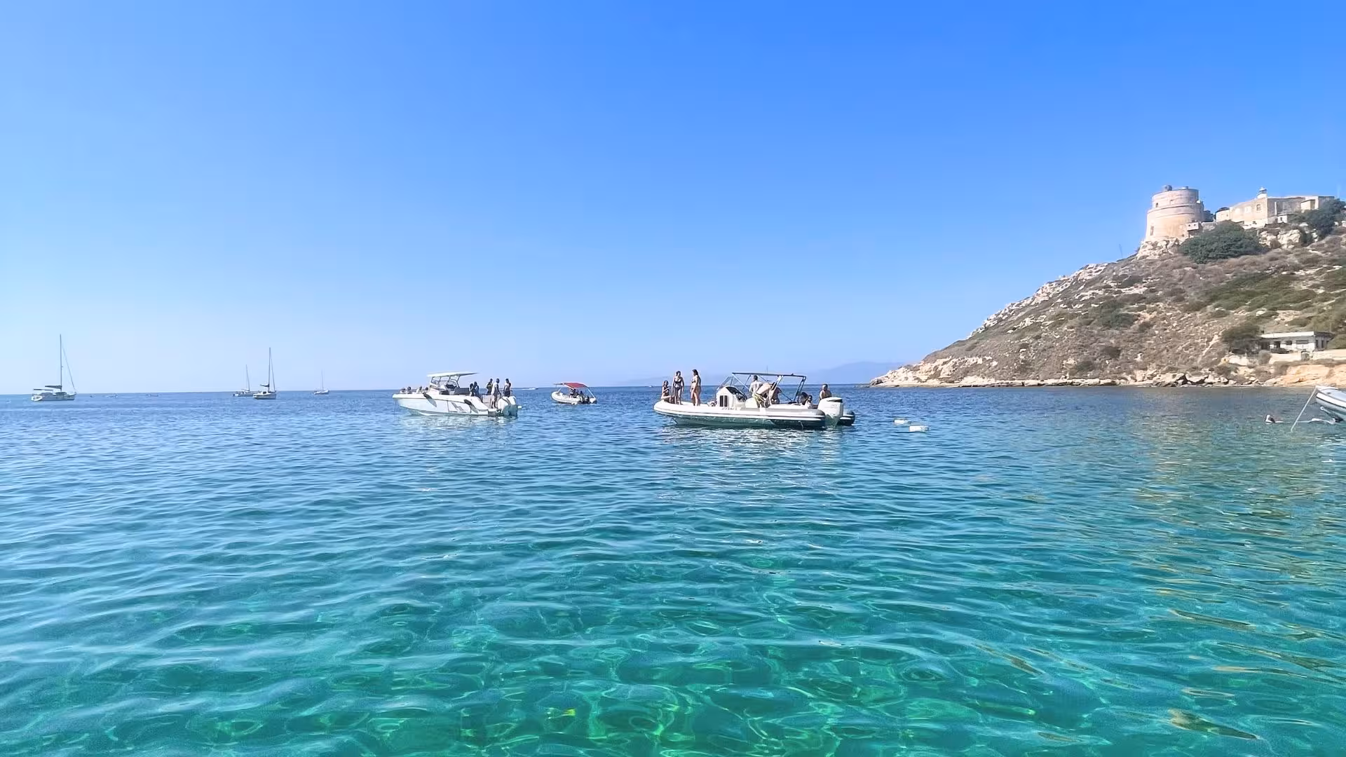 Scenic view of Cagliari's coastline with dinghies and a historic tower, ideal for snorkeling tours.