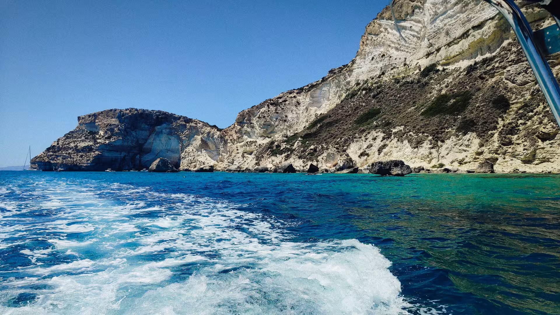 Dinghy cruising along Cagliari's stunning cliffs and turquoise waters on a sunny day.