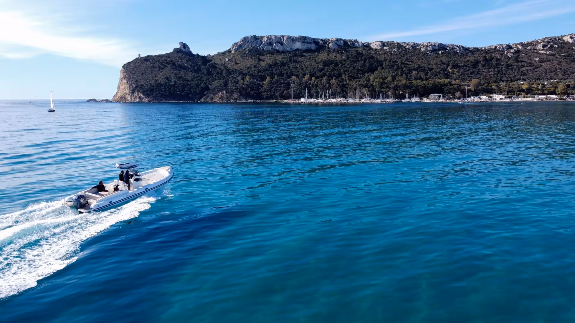 Dinghy cruising through the vibrant blue waters of the Gulf of Angels, Cagliari, with scenic cliffs in the background.