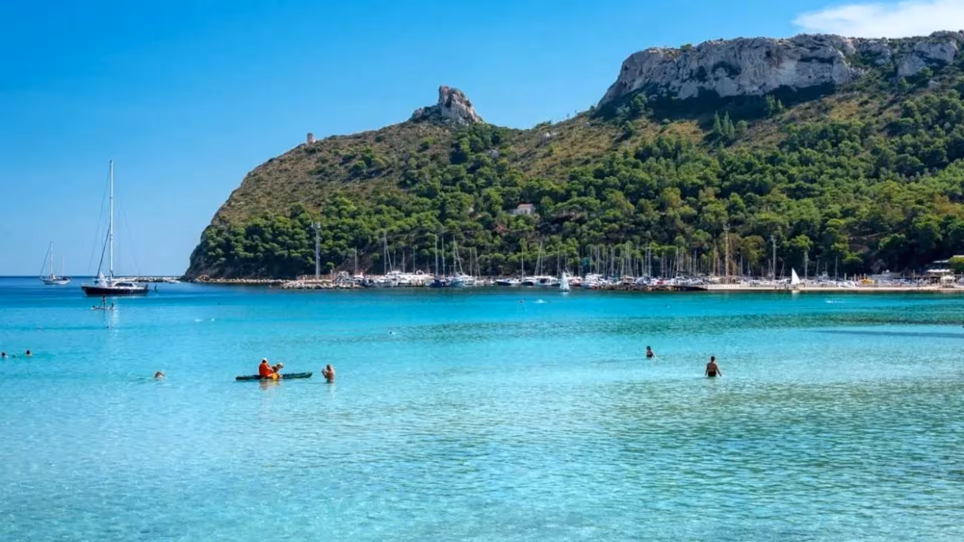 People enjoying water activities in the turquoise waters of the Gulf of Angels, surrounded by lush green hills in Cagliari.