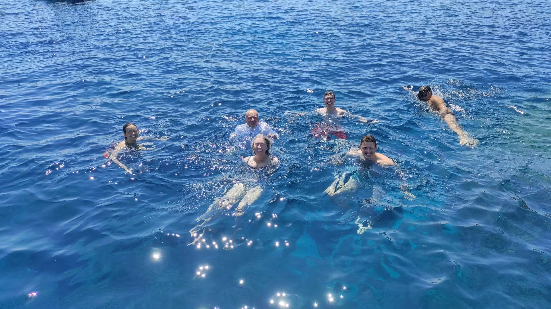 Group of happy tourists enjoying a refreshing swim in the clear blue sea during a Cagliari dinghy tour.