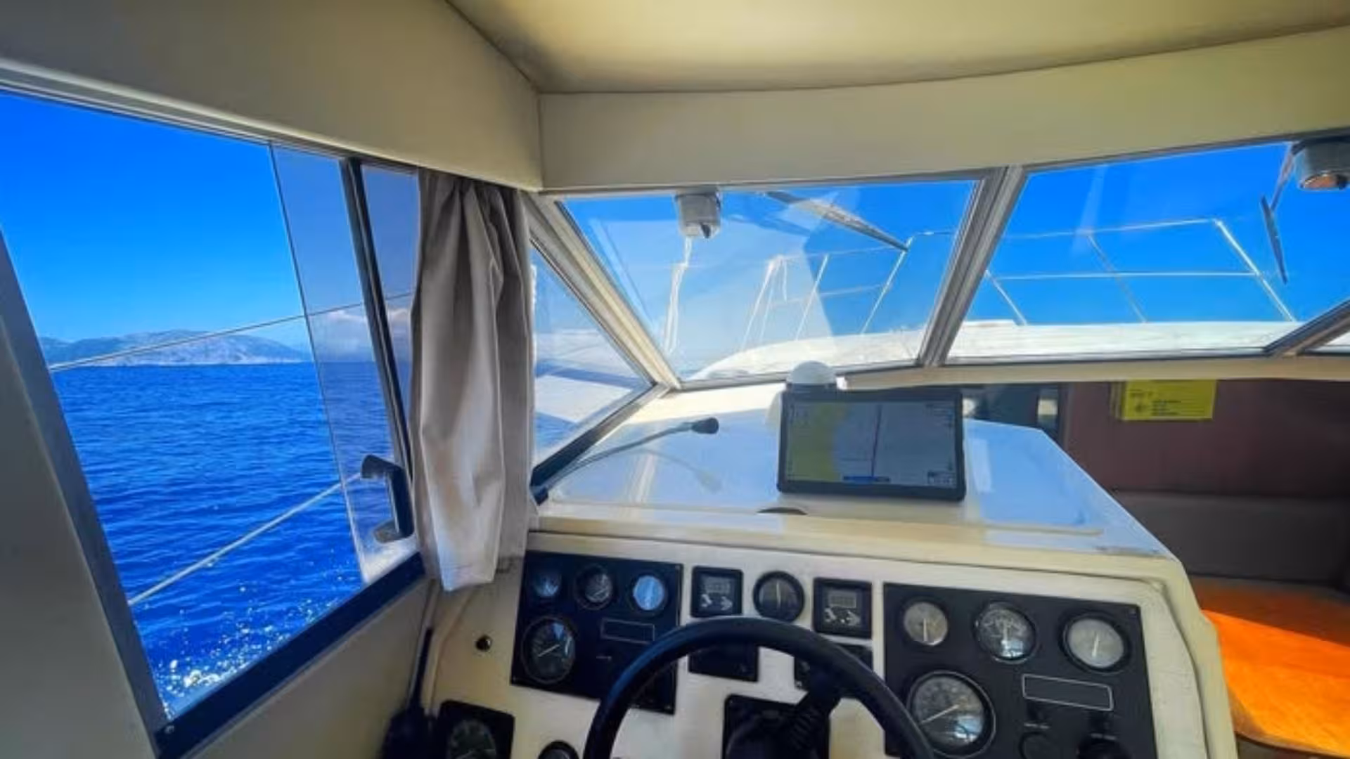 View from the helm of a tour boat cruising the Gulf of Angels, showcasing the clear blue Mediterranean Sea.