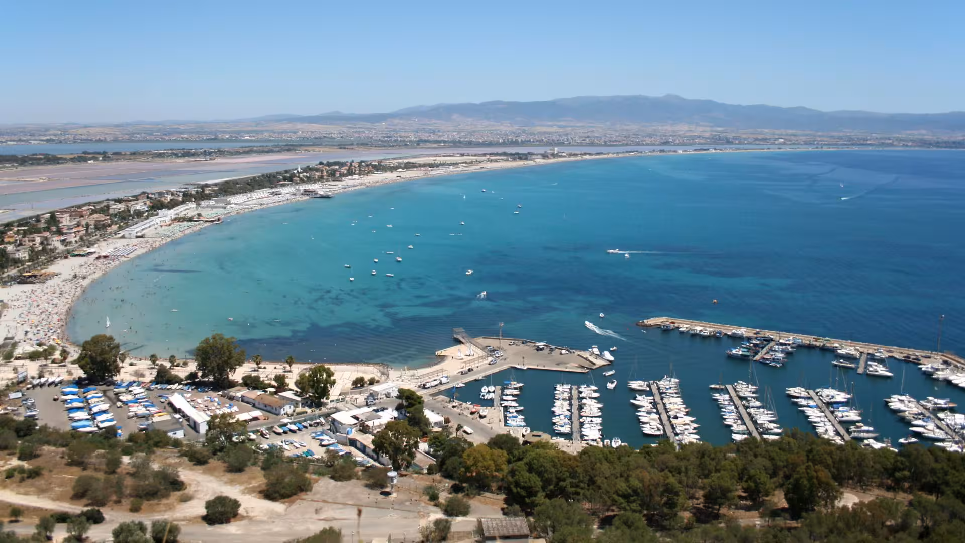 Panoramic view of Cagliari's coastline featuring a bustling marina and the expansive Gulf of Angels under a clear sky.