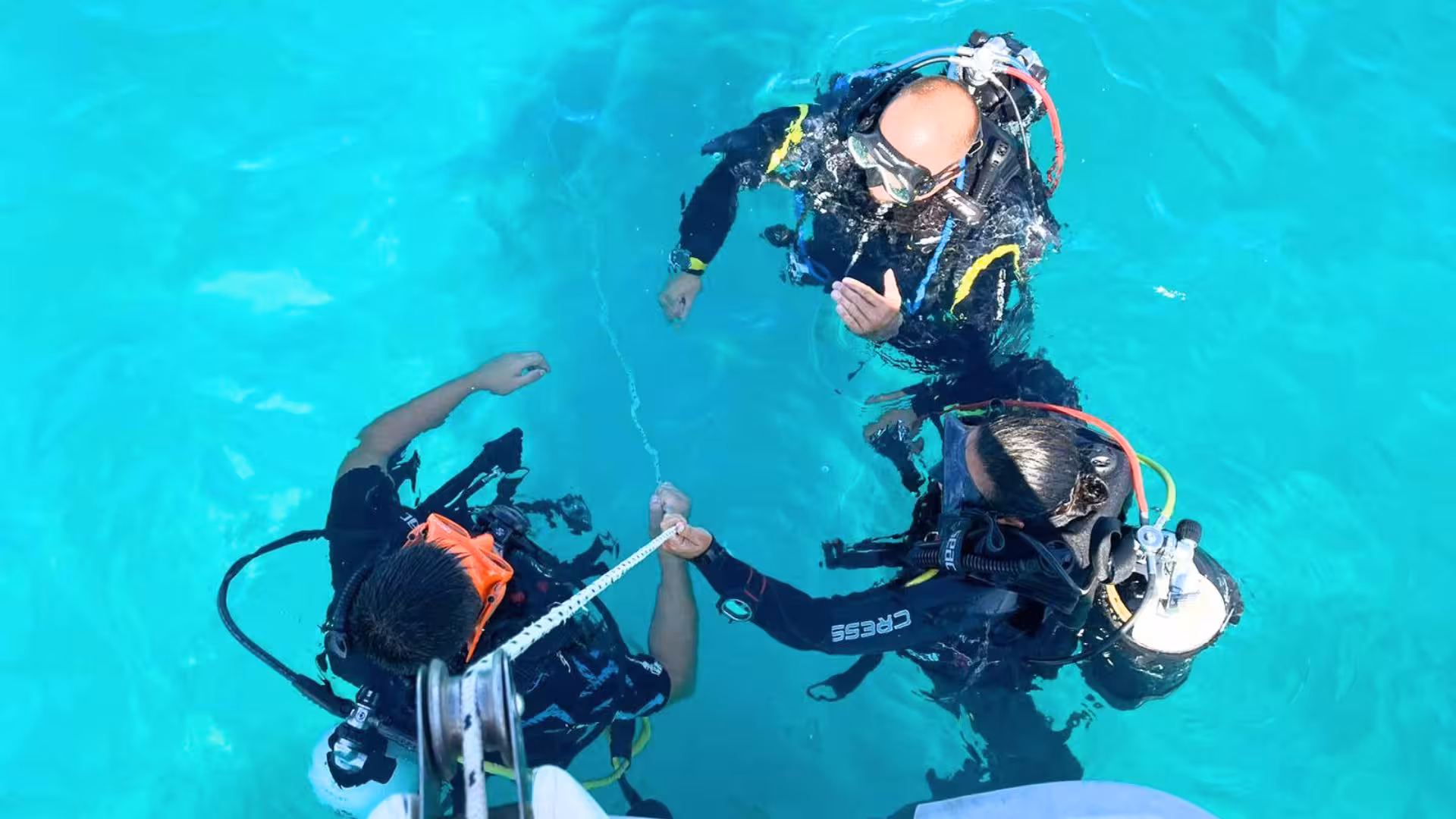 Three scuba divers preparing in crystal-clear waters for a dive in Cagliari's Gulf of Angels.
