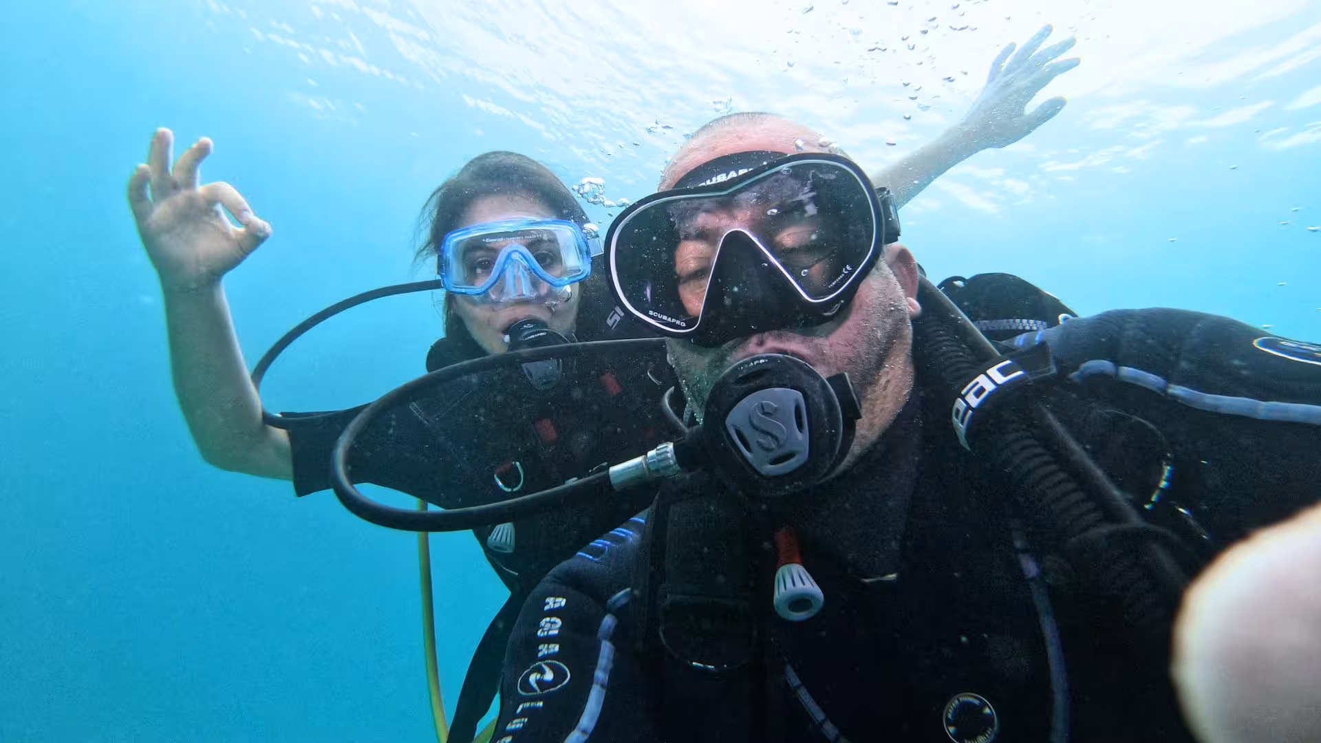 Two scuba divers giving the okay sign while exploring the vibrant marine life in Cagliari's Gulf of Angels.