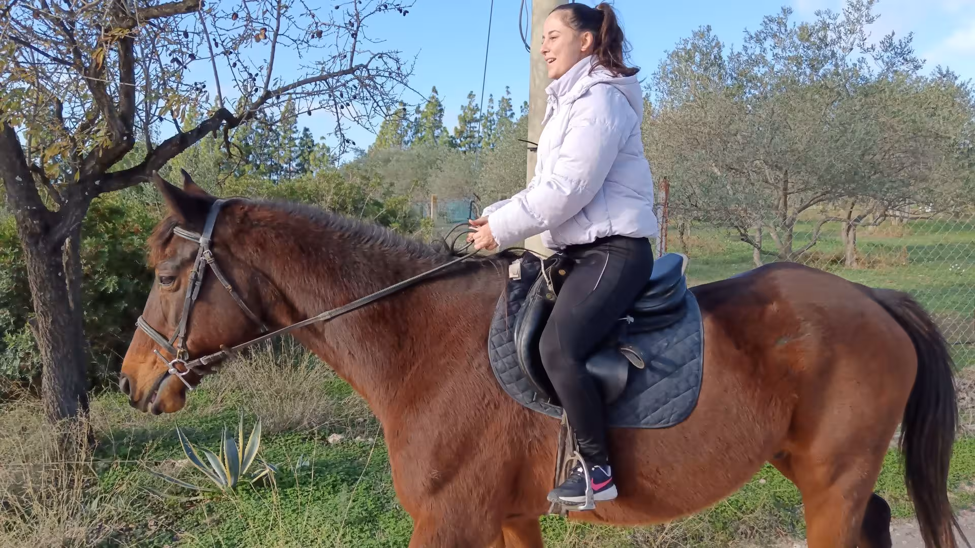 Woman enjoying a scenic horseback ride in Cagliari, surrounded by lush greenery and a clear blue sky.