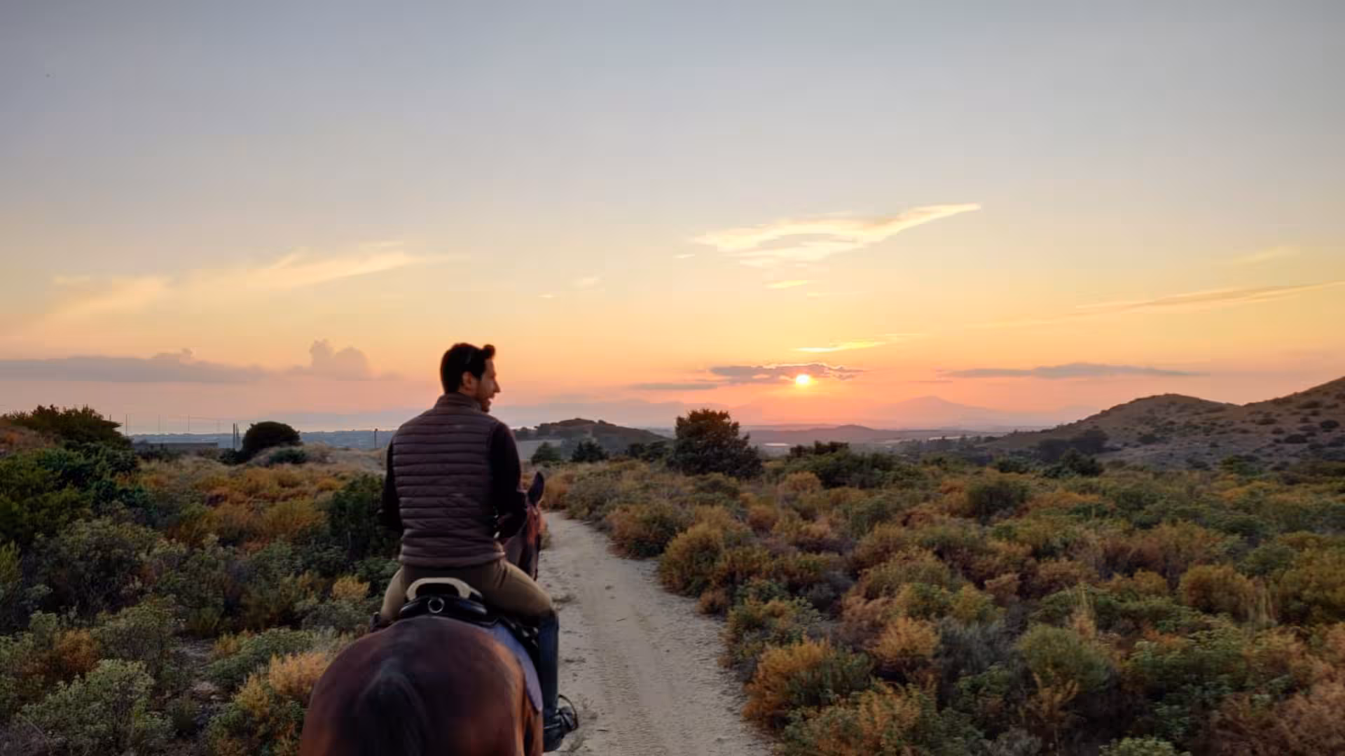 Rider on horseback admires a stunning sunset over Cagliari landscapes on a serene trail ride.