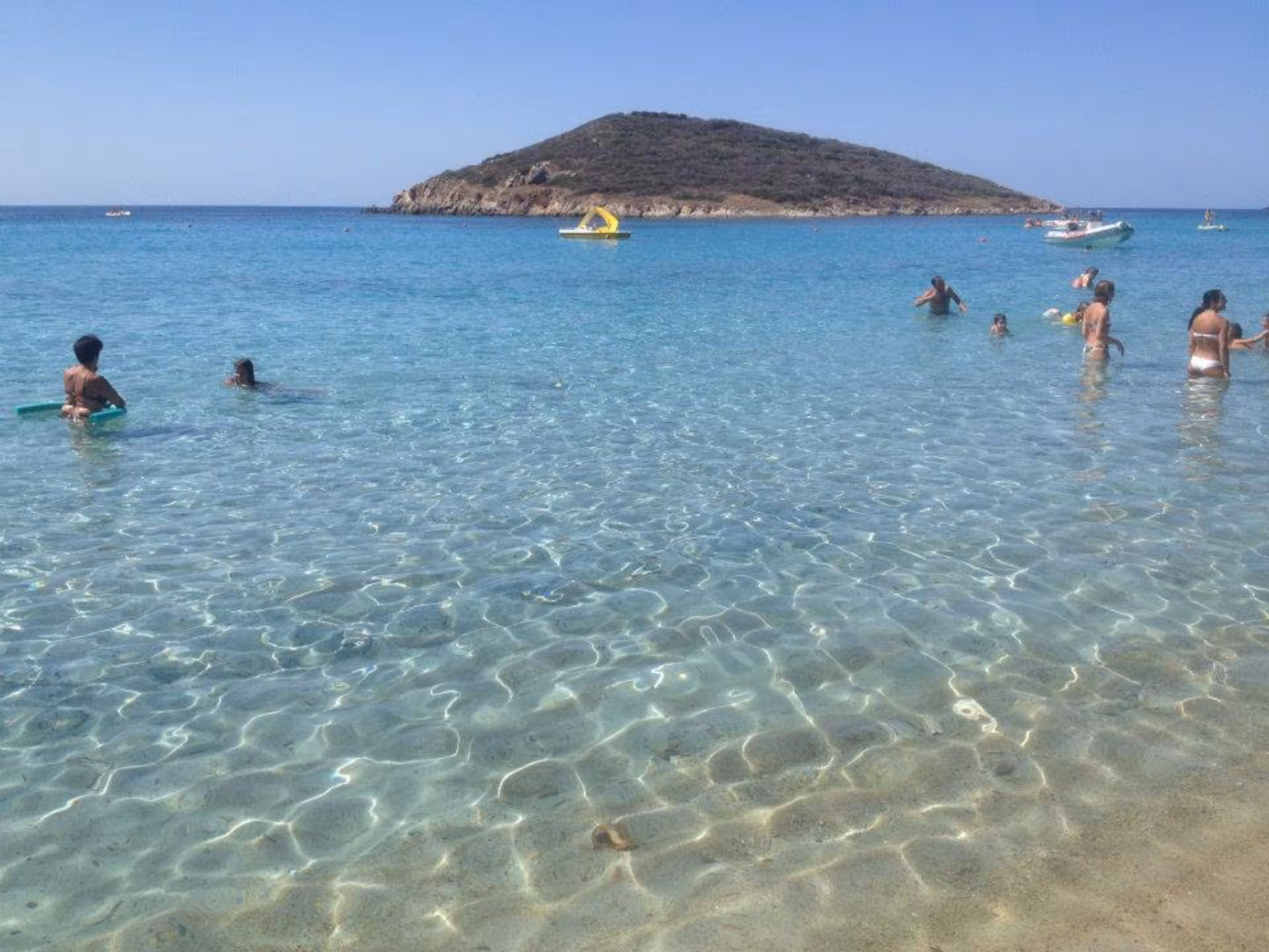 Visitors swimming in the crystal-clear waters at Chia Beach, showcasing the stunning scenery on the Cagliari jeep tour.