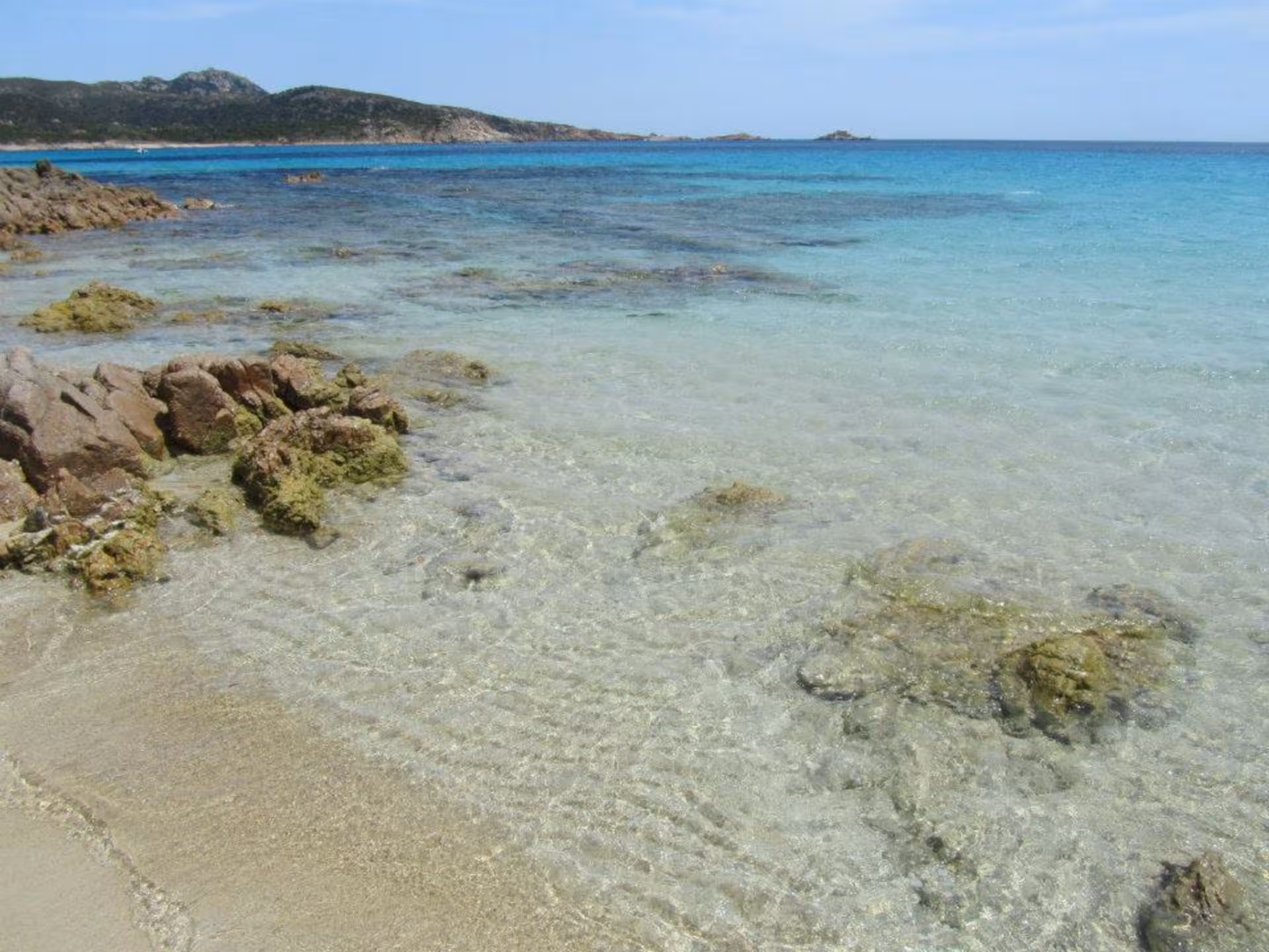 Crystal-clear waters and rocky shoreline of Chia beach on a sunny day, perfect for a jeep tour from Cagliari.