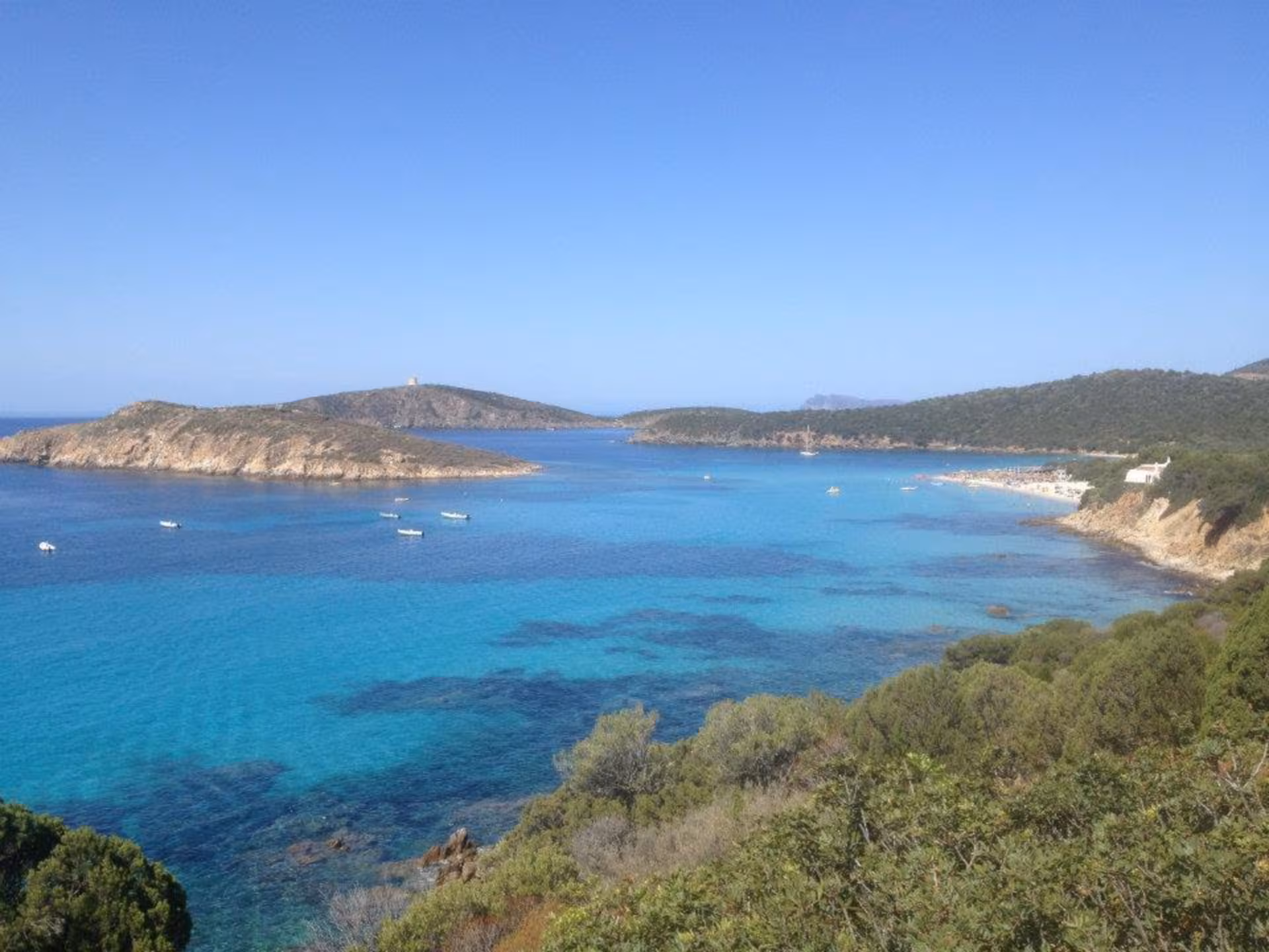 Stunning view of Chia's turquoise waters and rugged coastline on a sunny day, ideal for a jeep tour from Cagliari.