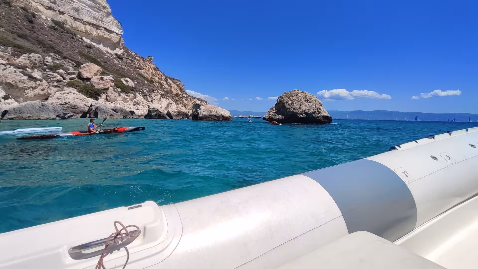 Kayakers paddling near rocky cliffs in Cagliari's vibrant blue waters during a dinghy tour.