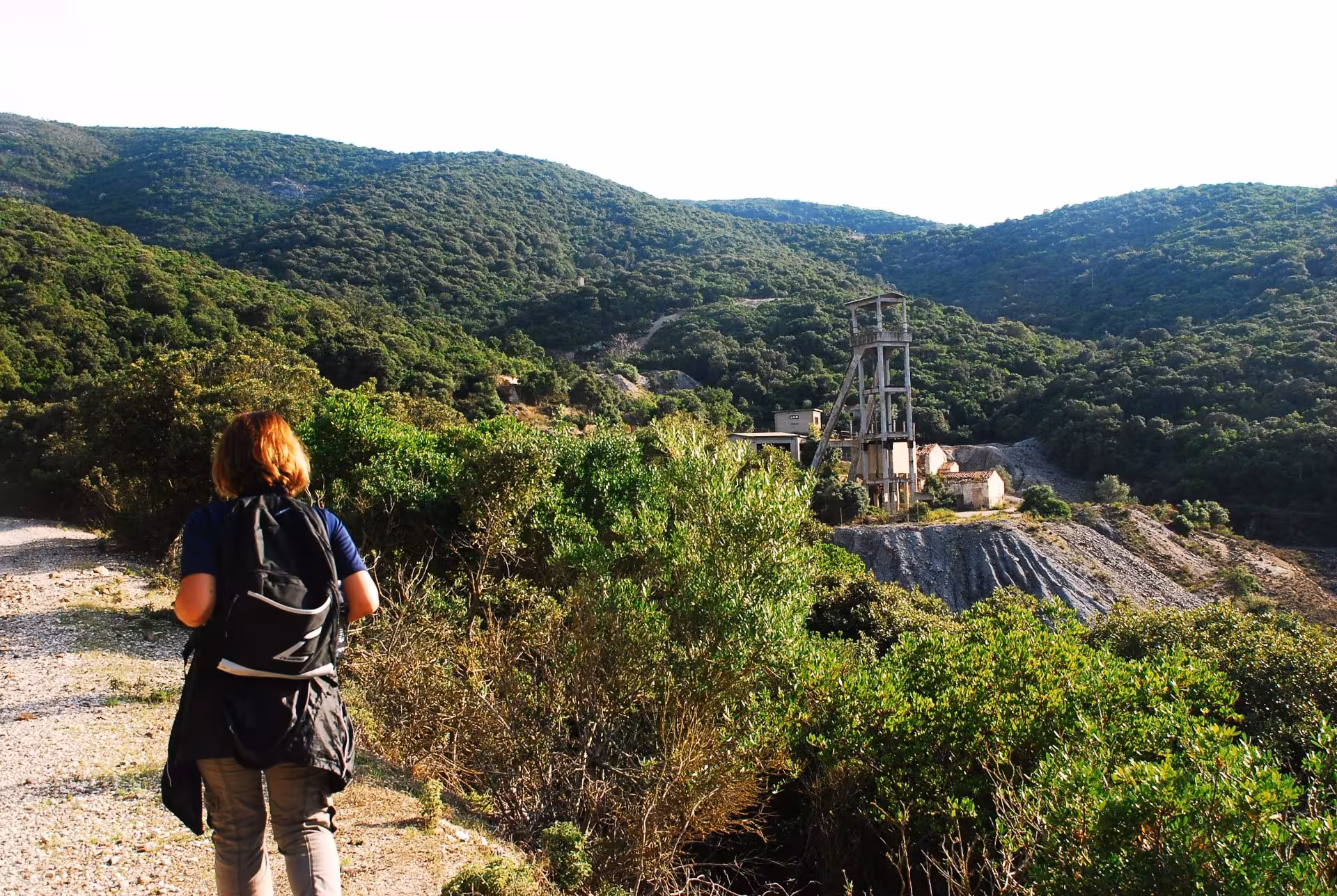 Hiker exploring the lush green hills and historic mining structures near Piscinas on a guided tour from Cagliari.