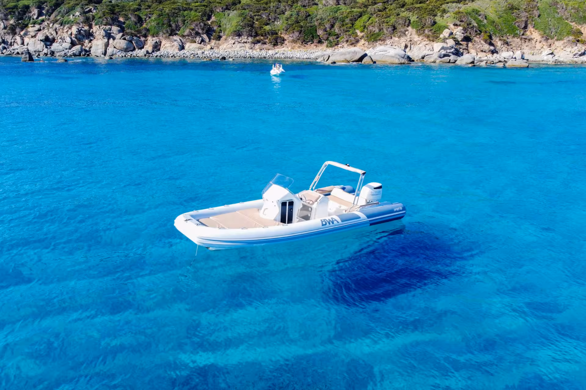 Pristine blue waters of Cagliari with a white RIB boat anchored near a lush, rocky shoreline.