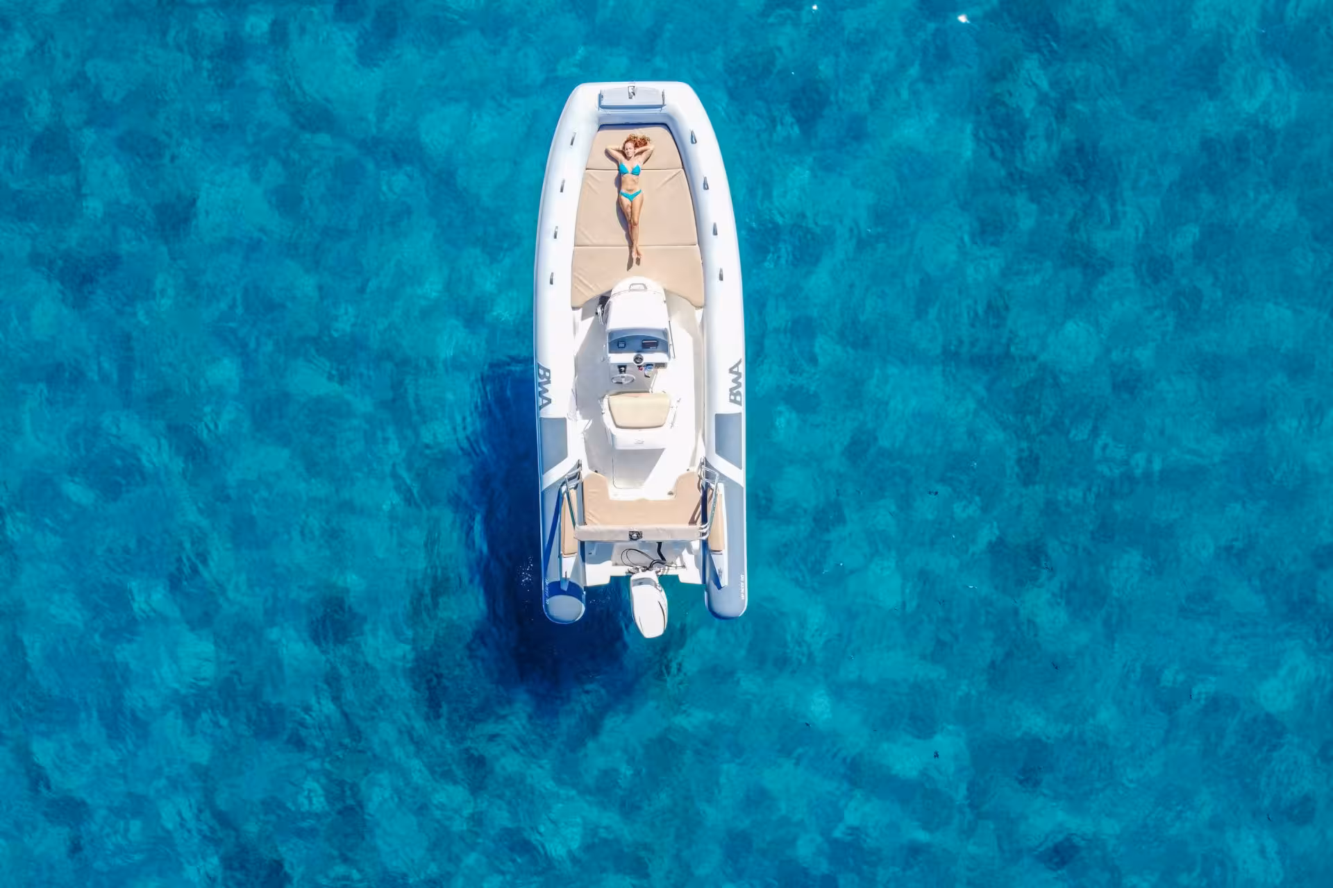 Aerial view of a RIB boat in Cagliari with a woman sunbathing on turquoise Mediterranean waters.