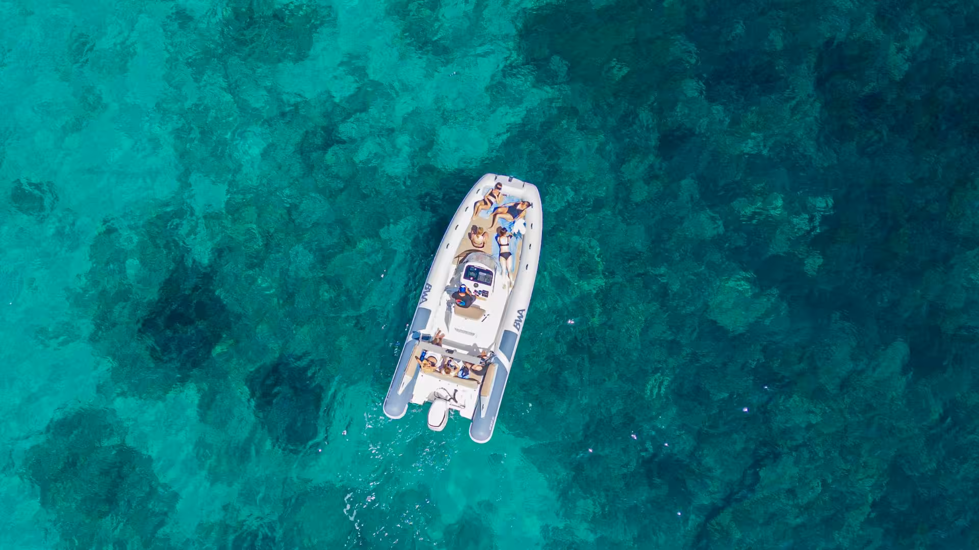 Aerial view of a RIB boat with sunbathers enjoying the crystal-clear waters off Cagliari.