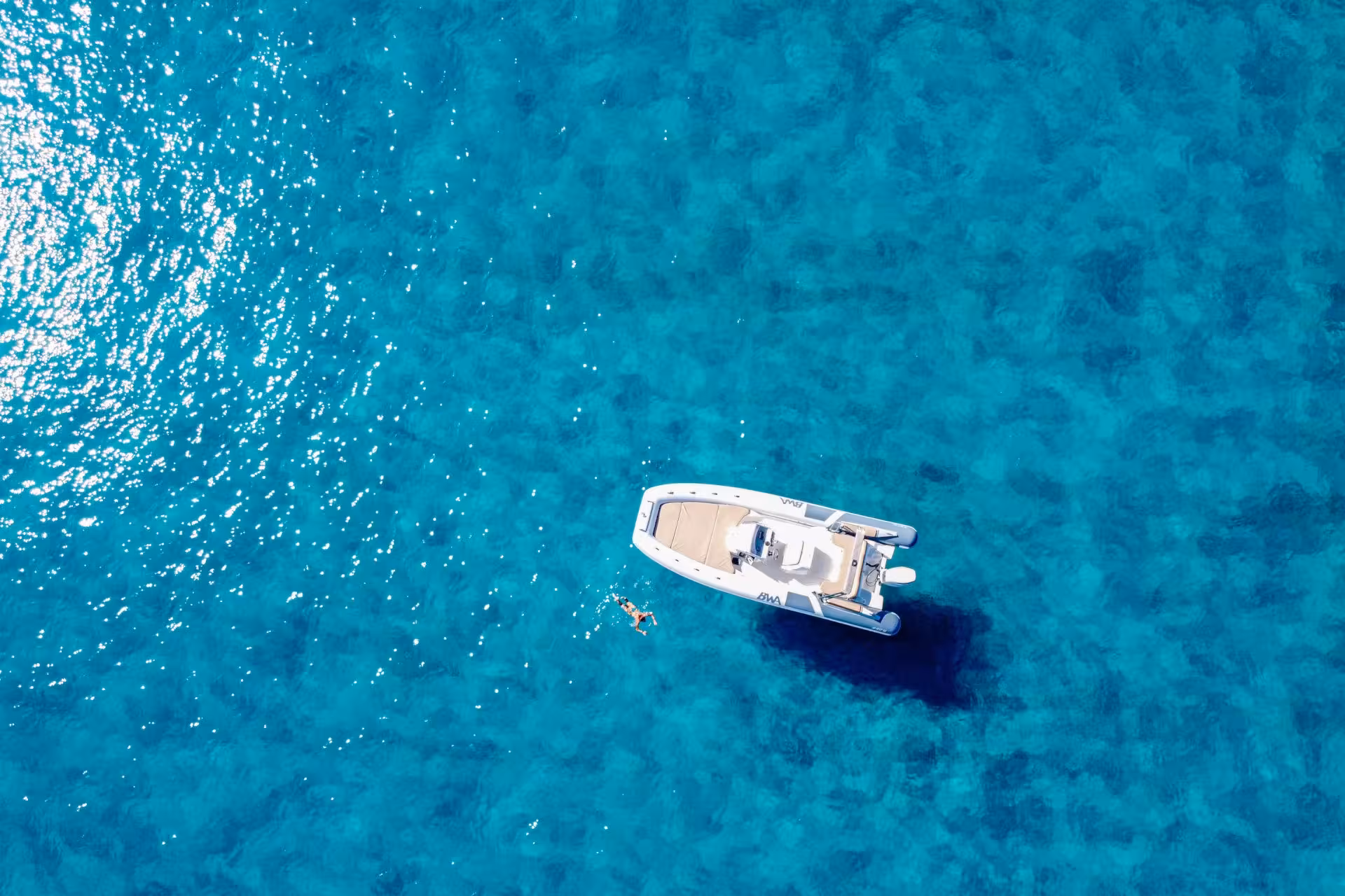 RIB boat floating on clear blue waters of Cagliari with a swimmer enjoying the serene sea.