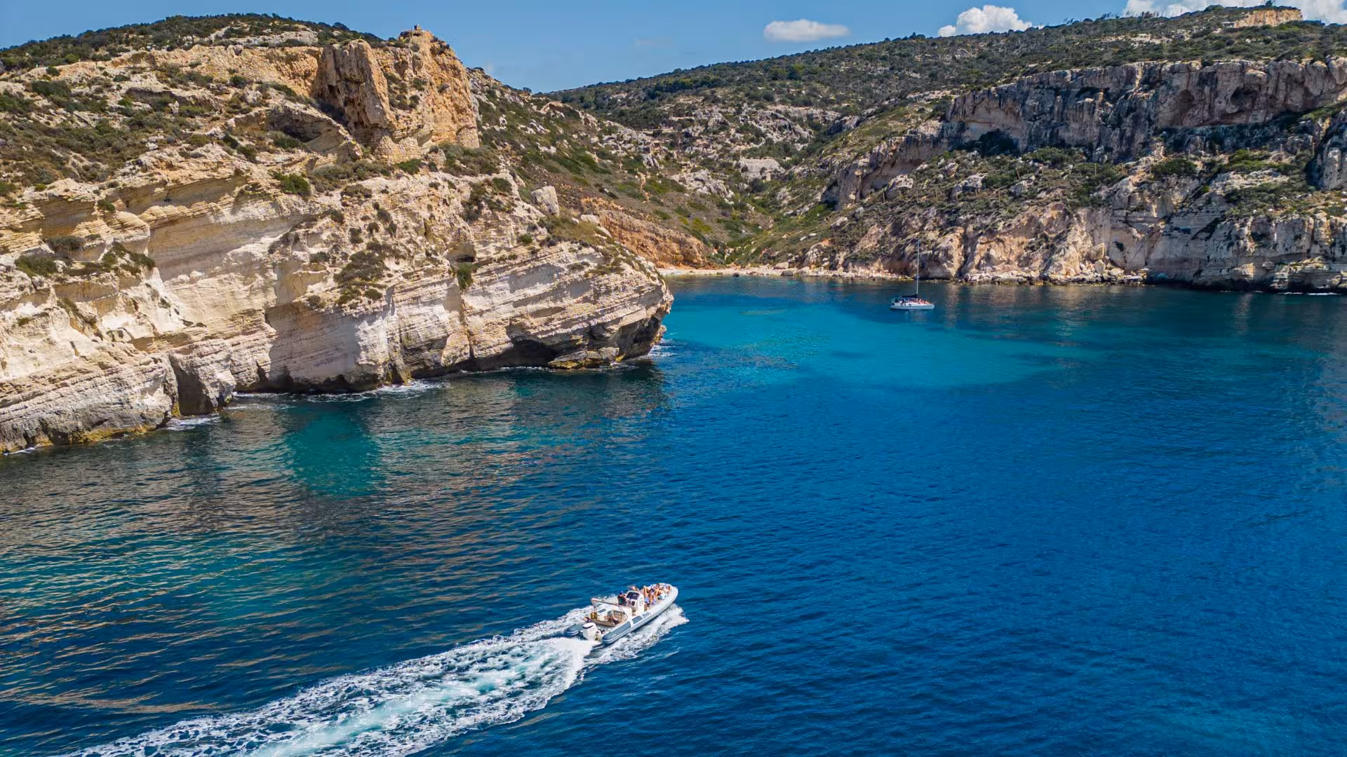 RIB boat cruising along the rugged cliffs and turquoise waters on a sunny Cagliari tour.