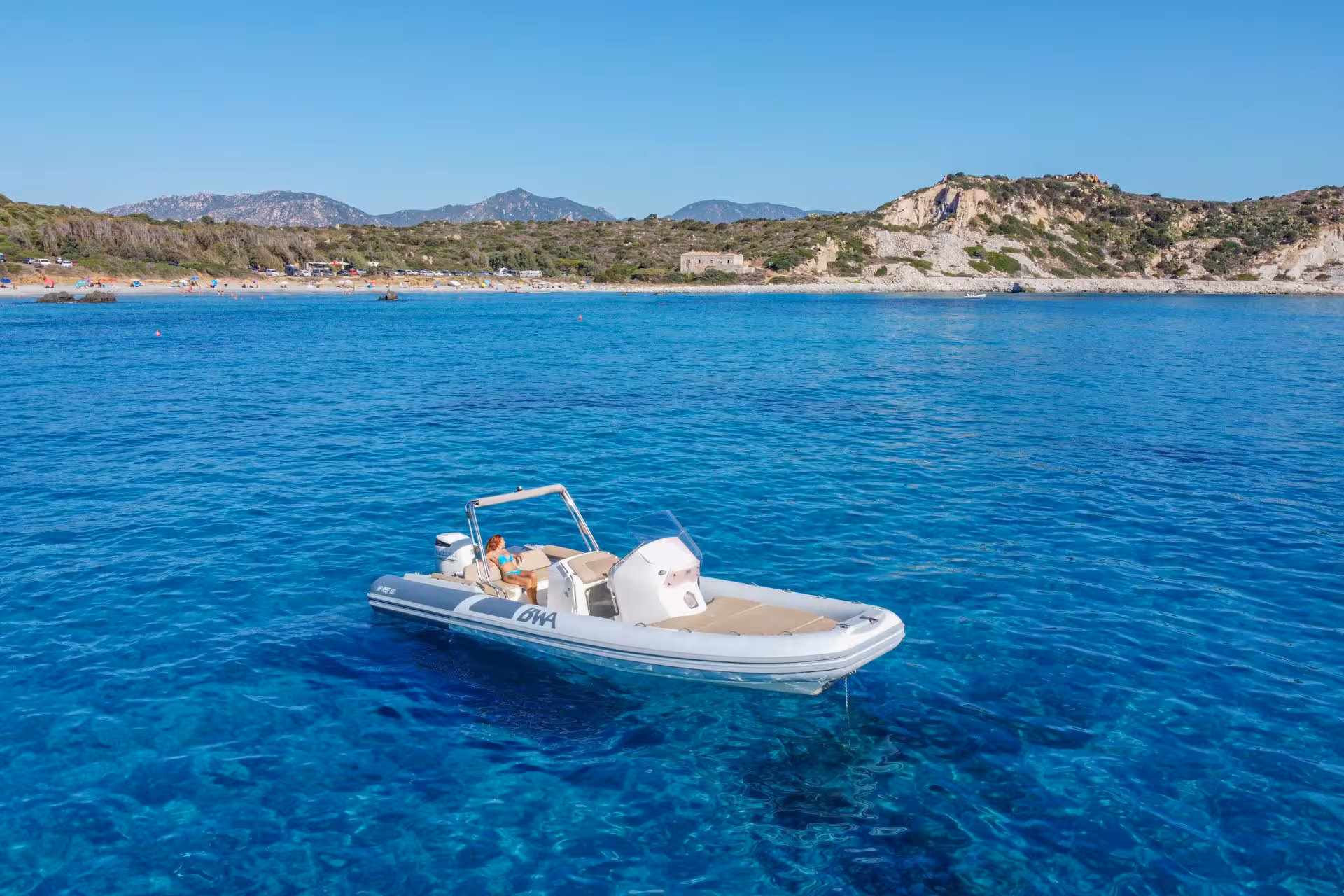 RIB boat floating on calm blue waters with a picturesque Cagliari coastline and mountains in the background.