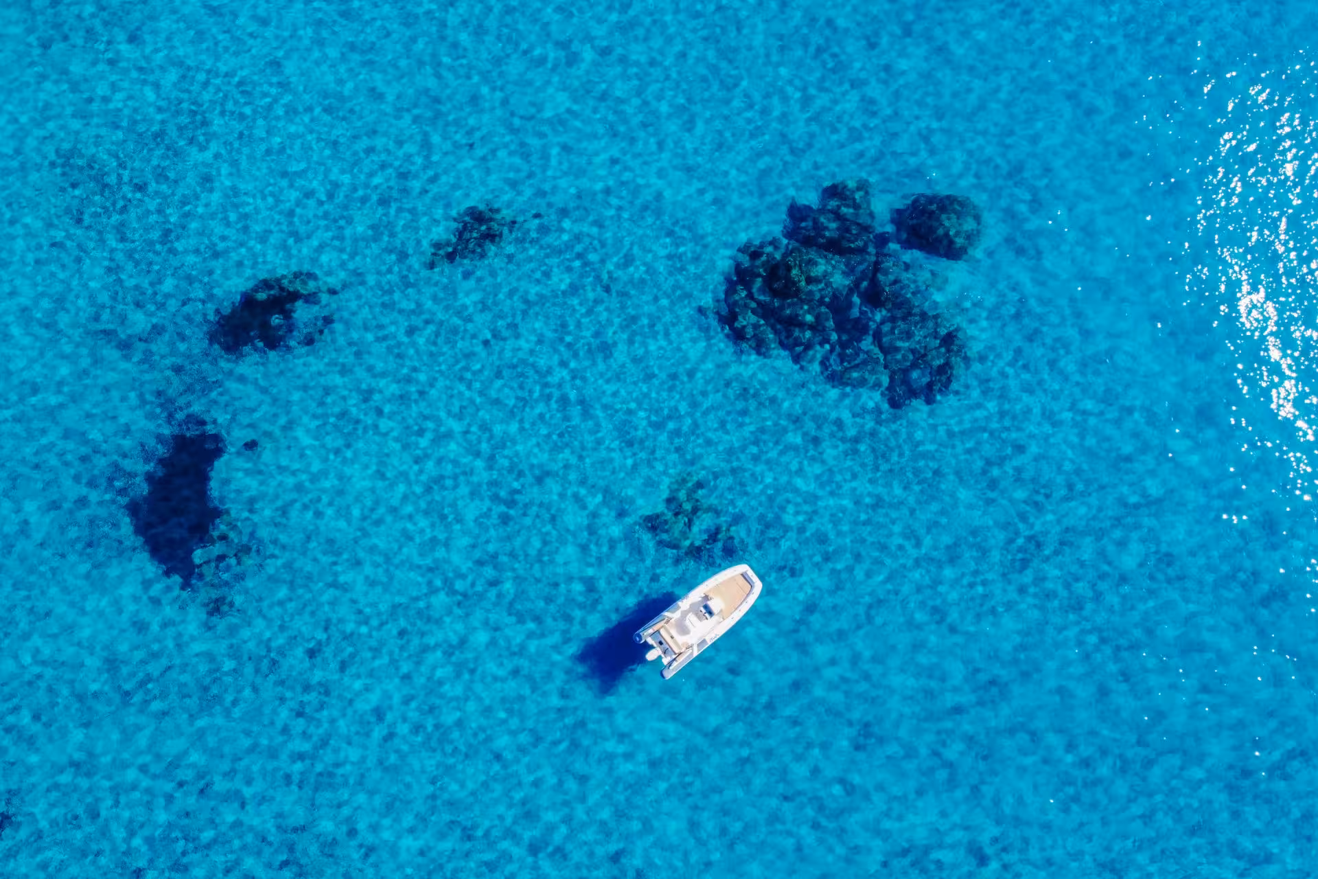 Aerial view of a RIB boat gliding over the crystal-clear turquoise waters near Cagliari, revealing vibrant marine life.