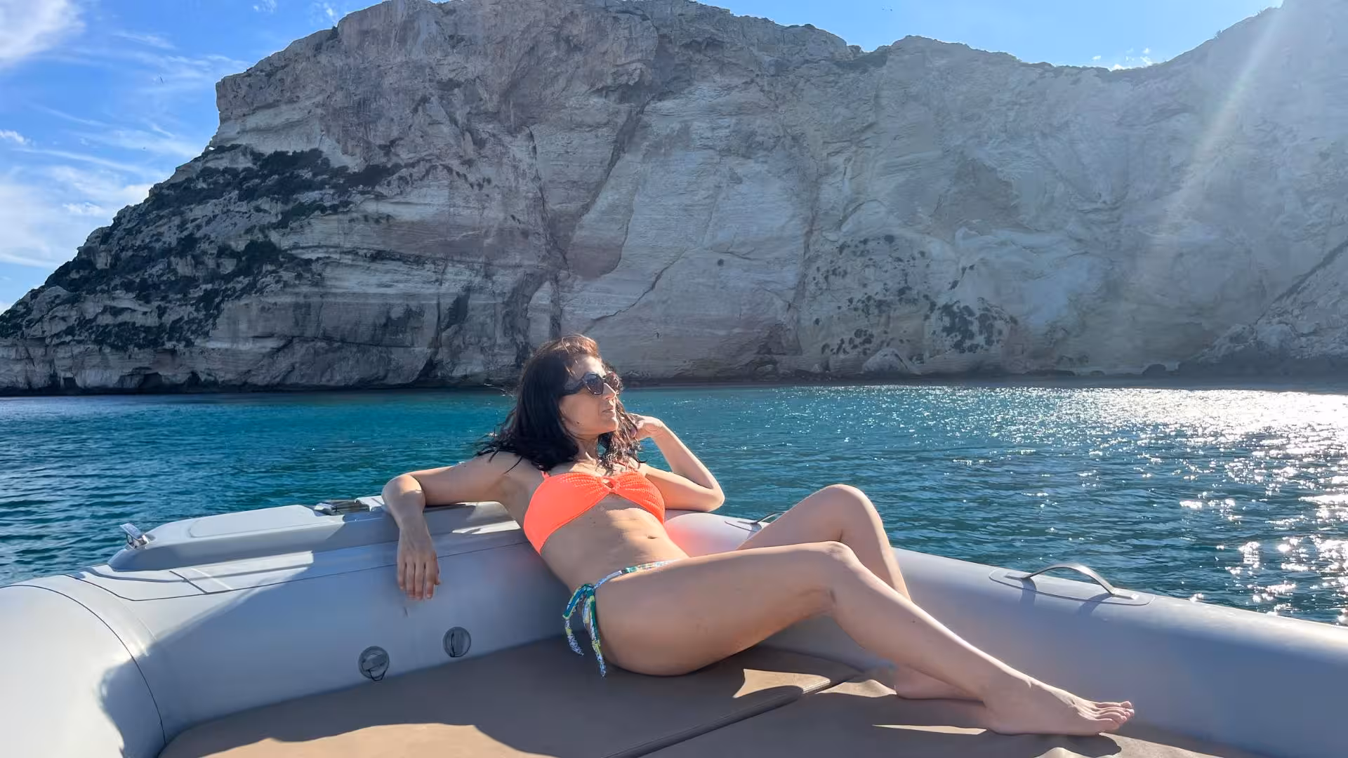Relaxing on a RIB tour in Cagliari with stunning cliffs and turquoise waters under a bright blue sky.
