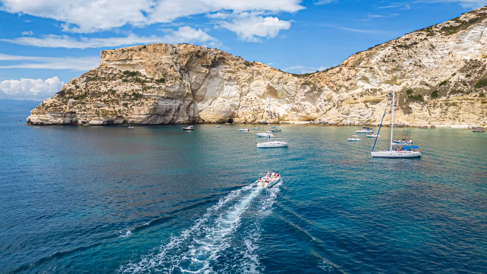 Scenic RIB tour near Cagliari showcasing sailboats and rocky coastline under a bright blue sky.