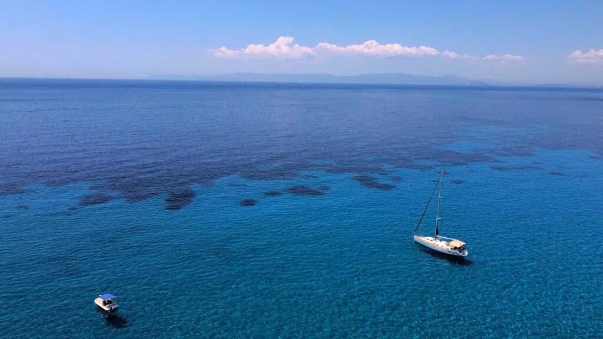 Sailing boat glides on crystal-clear waters near Mari Pintau, Cagliari, offering stunning views and a serene experience.