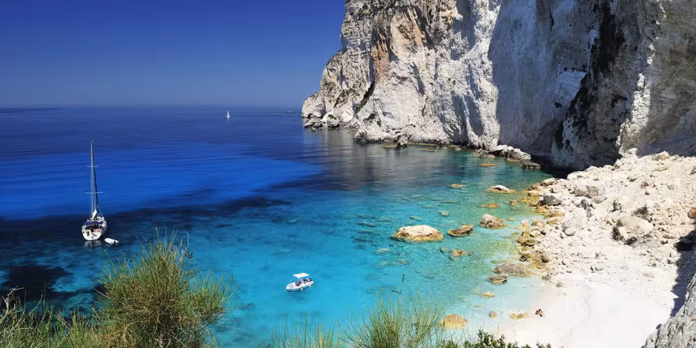 Stunning view of a sailing boat near the rocky cliffs and turquoise waters of Cagliari’s coastline on a sunny day.