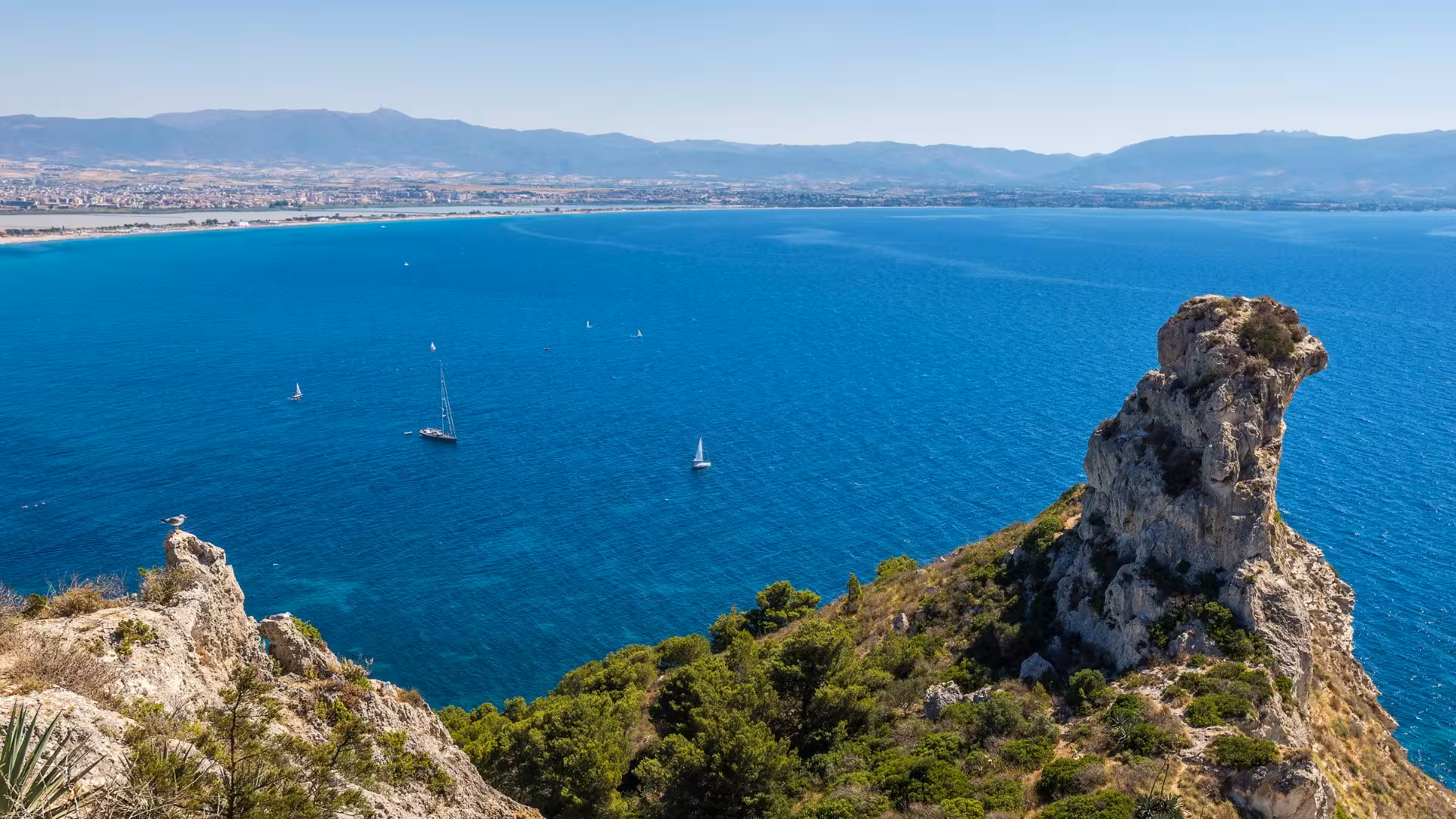 Scenic view of Sella del Diavolo with azure waters and sailboats near Cagliari, ideal for trekking adventures.