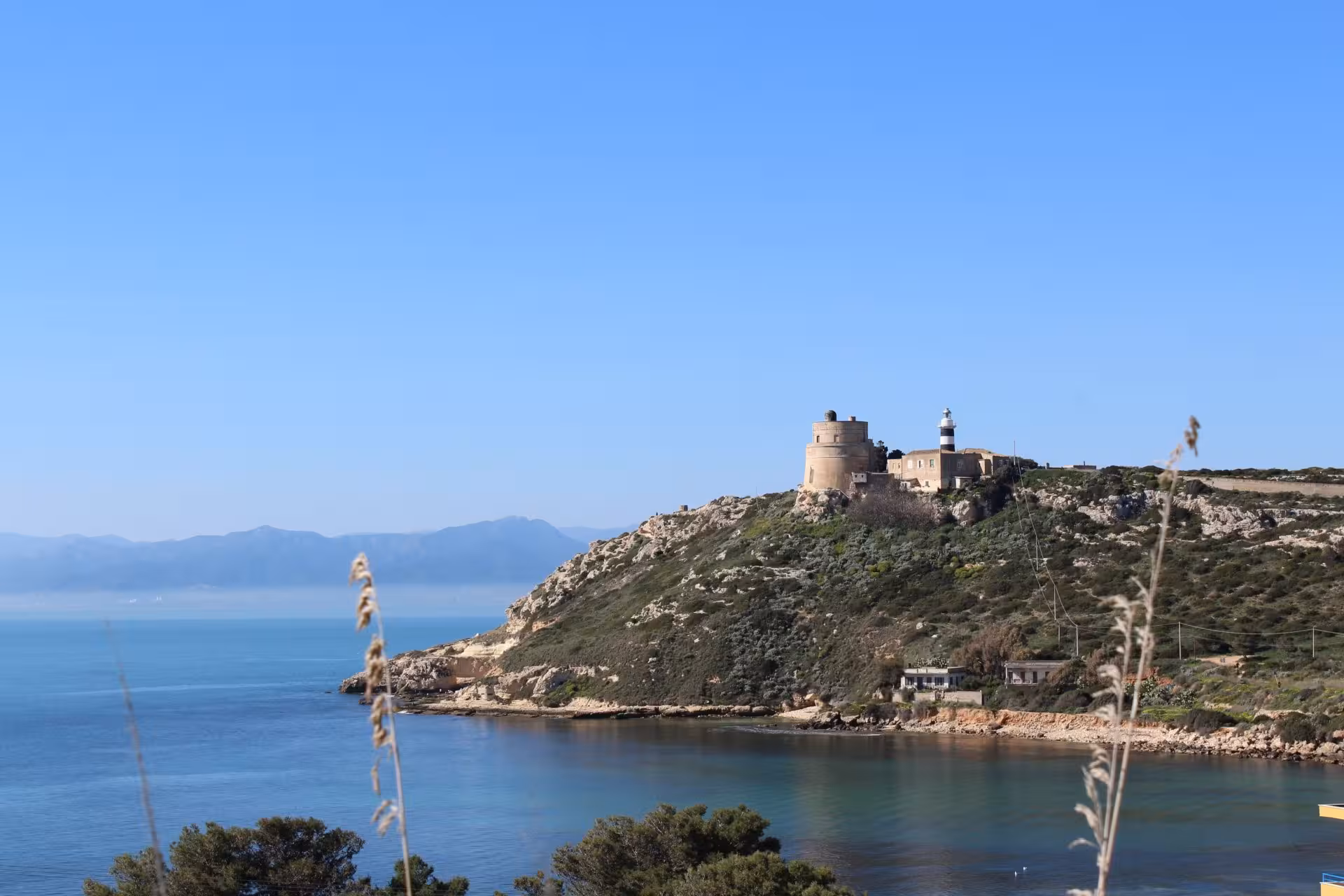 Scenic view of Sella del Diavolo in Cagliari with clear blue skies and a historic lighthouse overlooking the sea.