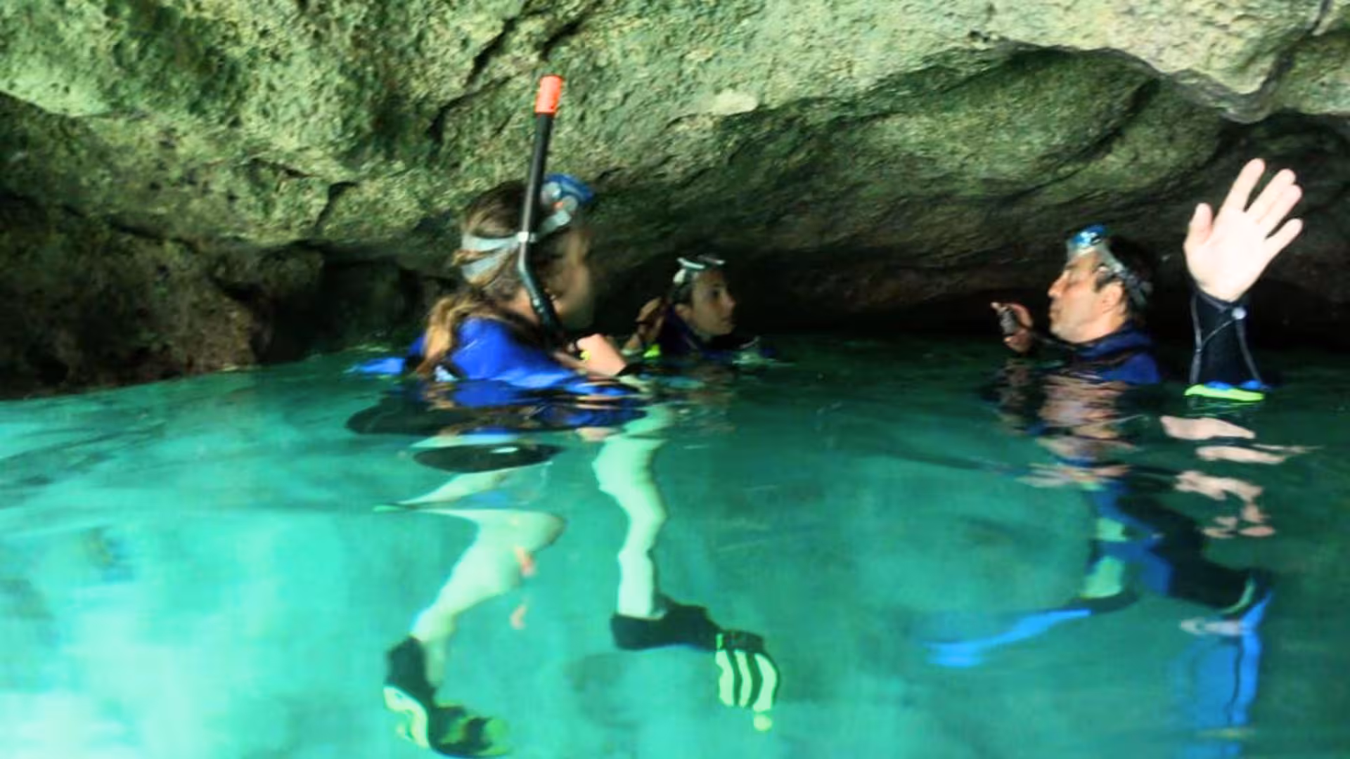 Group of snorkelers exploring a tranquil cave in Cagliari, guided through crystal-clear waters beneath rocky ceilings.
