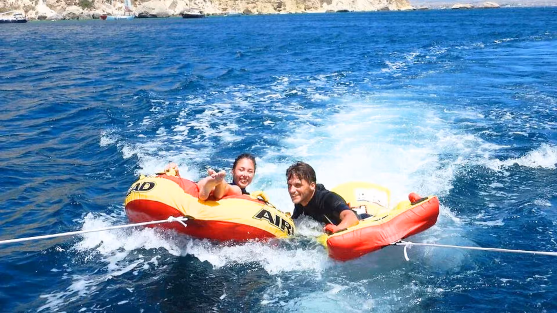 Two people enjoying thrilling tubing adventure in Golfo degli Angeli's clear blue waters.