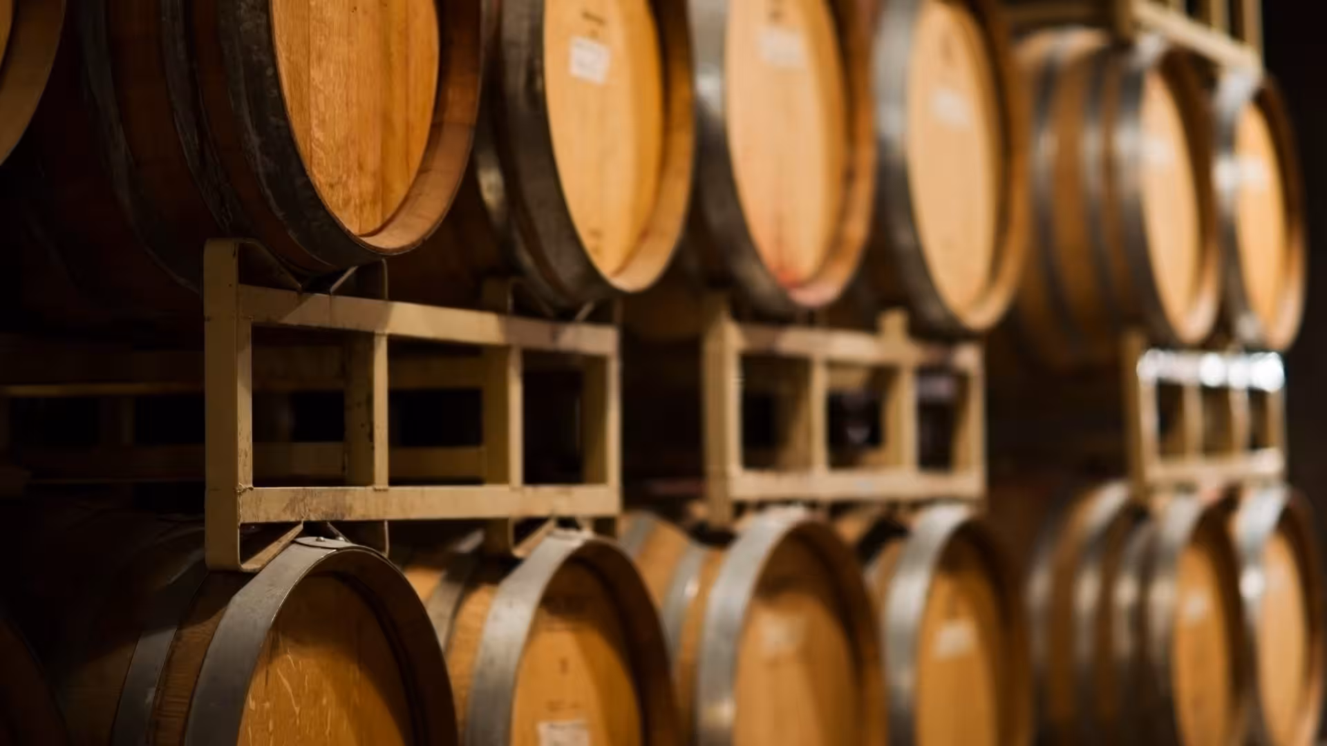 Close-up of wooden wine barrels aging in a dimly lit Cagliari cellar, ideal for wine enthusiasts.