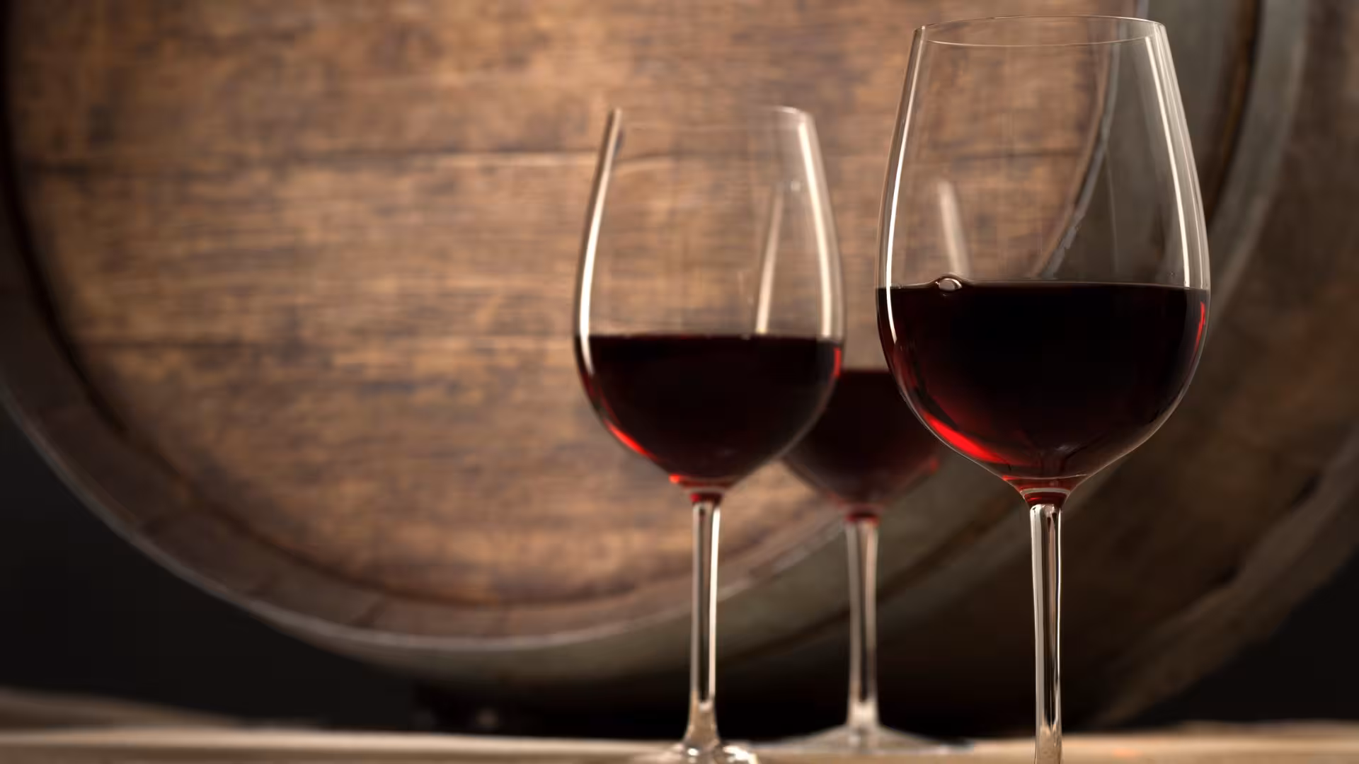 Three glasses of red wine in front of a wooden barrel at a Cagliari winery tasting tour.