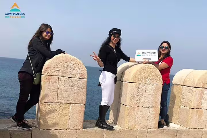 Travelers pose by Alexandria seafront fortress walls on Cairo to Abu Simbel 8 days 7 nights road tour