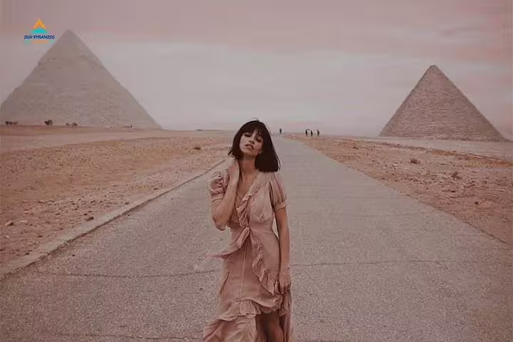Woman posing on Giza Plateau road with Great Pyramids behind, Cairo to Abu Simbel overland package